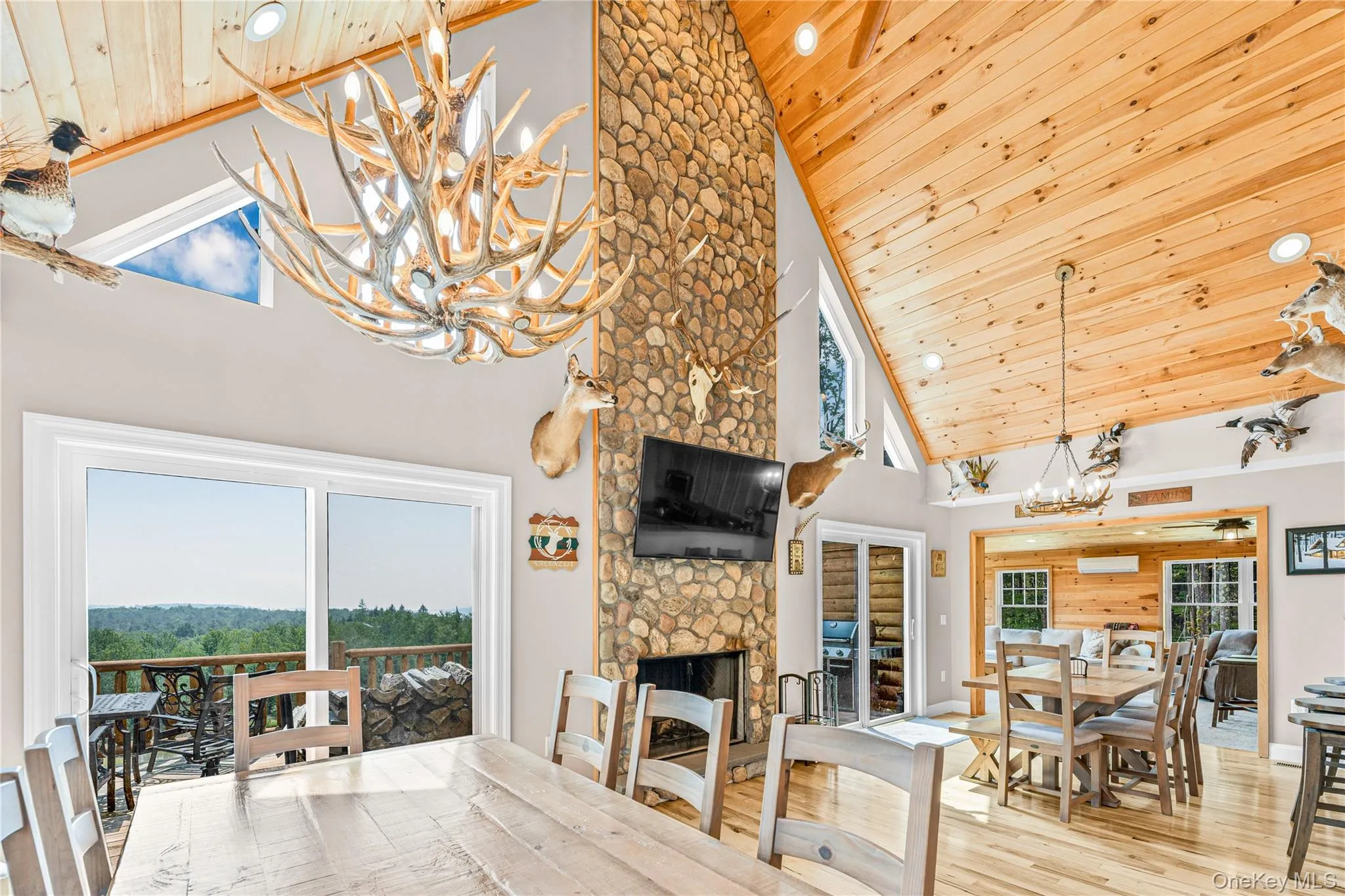 Dining area featuring a chandelier, a stone fireplace, high vaulted ceiling, wood ceiling, and wood finished floors Dining area featuring a chandelier, a stone fireplace, high vaulted ceiling, wood ceiling, and wood finished floors