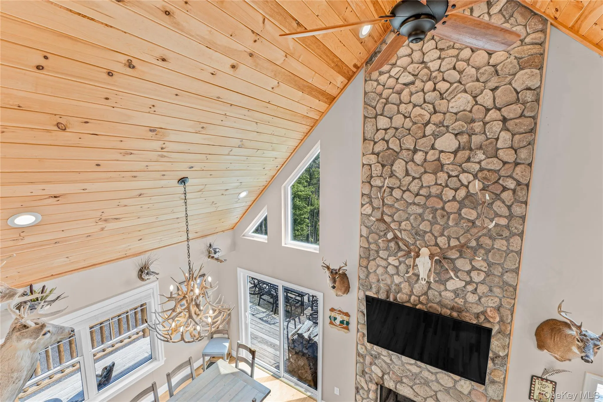 Living area featuring high vaulted ceiling, wood ceiling, a multi sided fireplace, a chandelier, and a ceiling fan Living area featuring high vaulted ceiling, wood ceiling, a multi sided fireplace, a chandelier, and a ceiling fan