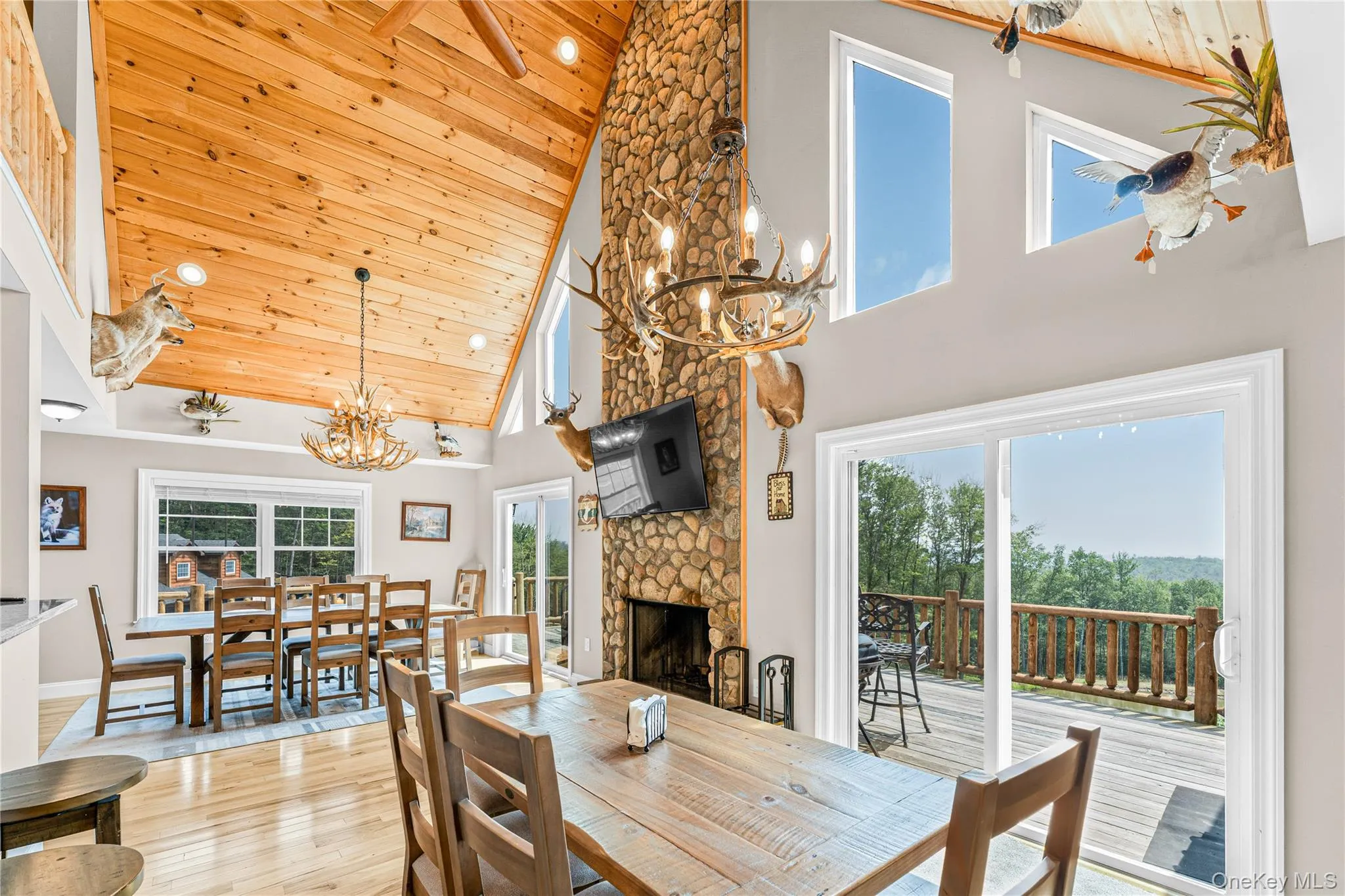Dining room with wooden ceiling, a chandelier, a stone fireplace, light wood-style floors, and high vaulted ceiling Dining room with wooden ceiling, a chandelier, a stone fireplace, light wood-style floors, and high vaulted ceiling