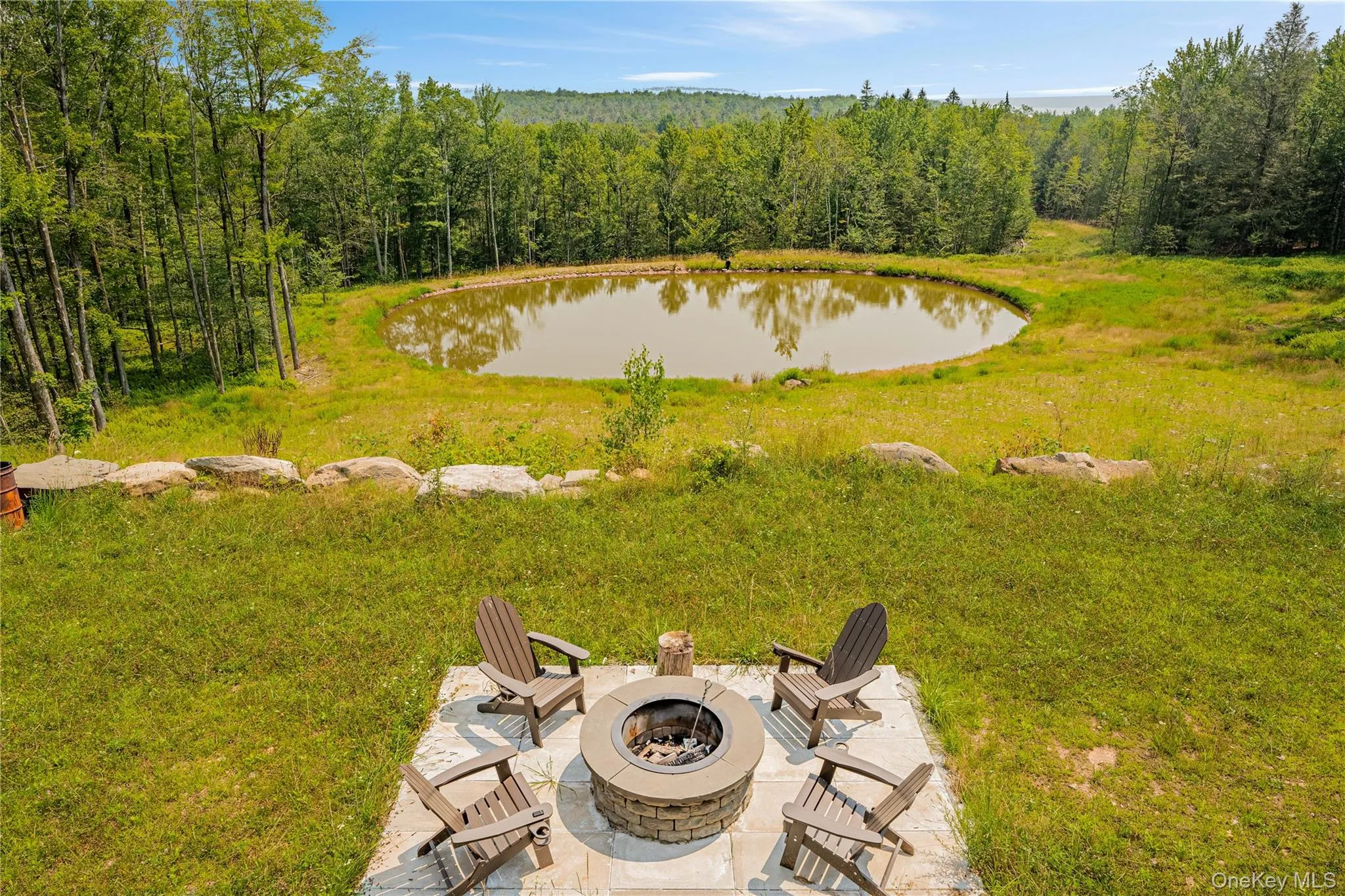 View of green lawn featuring a water view, a wooded view, a fire pit, and a patio area View of green lawn featuring a water view, a wooded view, a fire pit, and a patio area