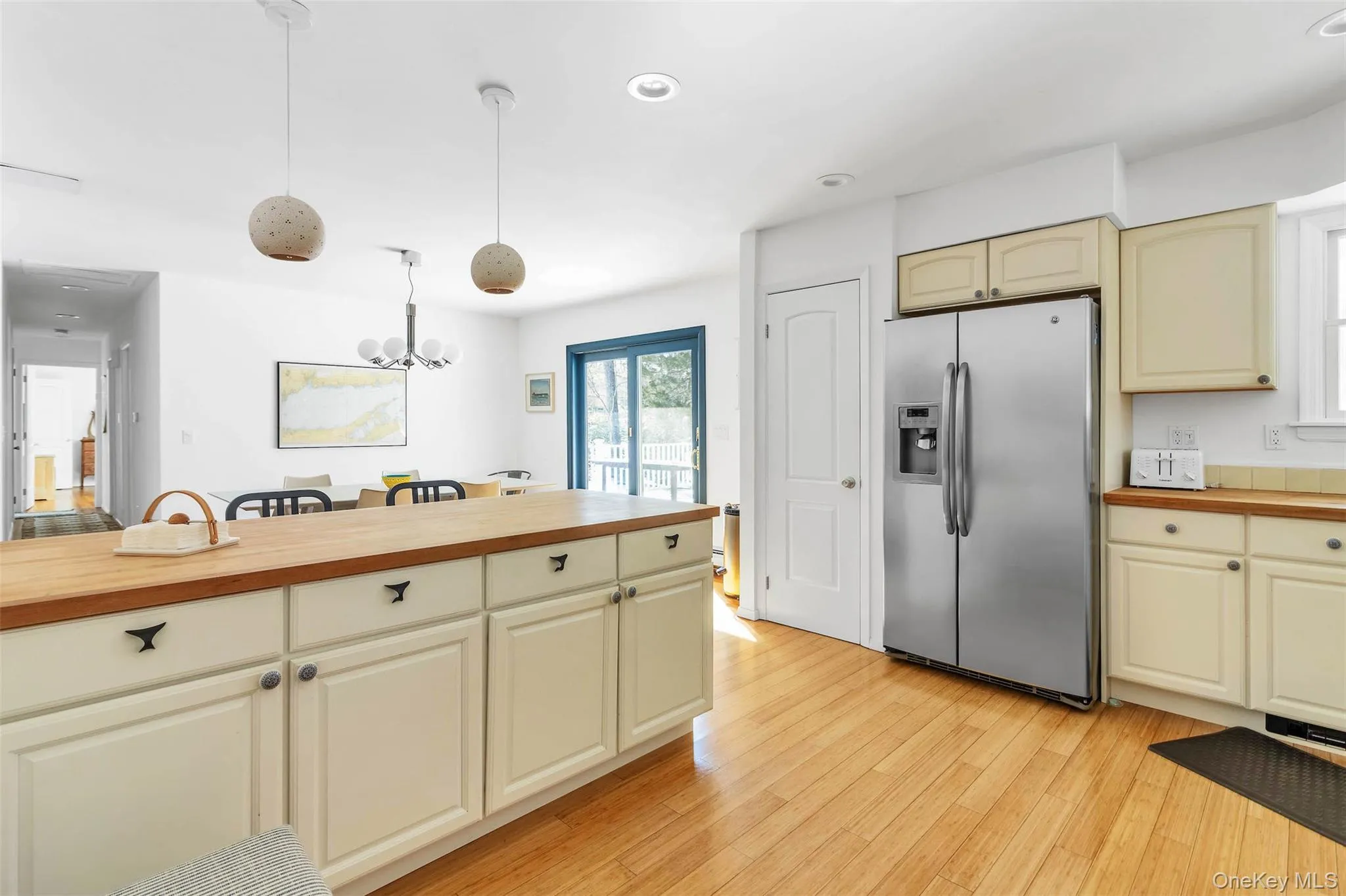 Kitchen with butcher block counters, hanging light fixtures, stainless steel fridge, light hardwood / wood-style floors, and cream cabinets Kitchen with butcher block counters, hanging light fixtures, stainless steel fridge, light hardwood / wood-style floors, and cream cabinets