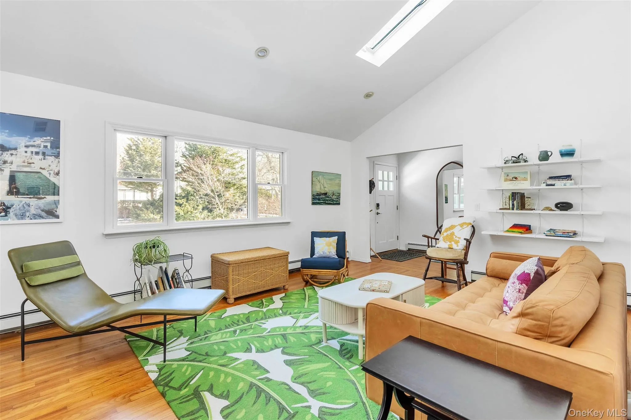 Living room with baseboard heating, high vaulted ceiling, a skylight, and hardwood / wood-style floors Living room with baseboard heating, high vaulted ceiling, a skylight, and hardwood / wood-style floors