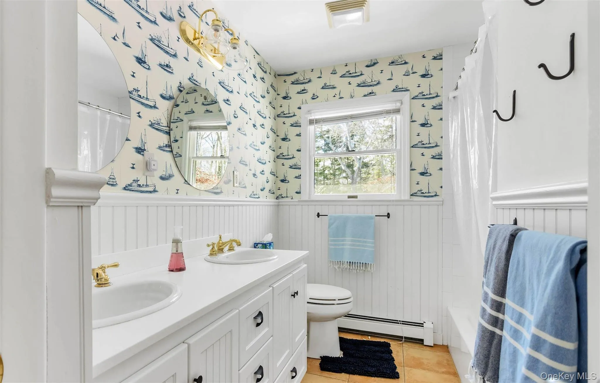 Full bathroom with toilet, vanity, shower / bath combo, tile patterned flooring, and a baseboard heating unit Full bathroom with toilet, vanity, shower / bath combo, tile patterned flooring, and a baseboard heating unit