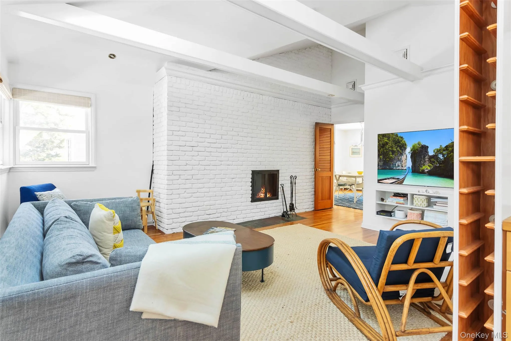 Living room with brick wall, beam ceiling, a brick fireplace, and light hardwood / wood-style flooring Living room with brick wall, beam ceiling, a brick fireplace, and light hardwood / wood-style flooring