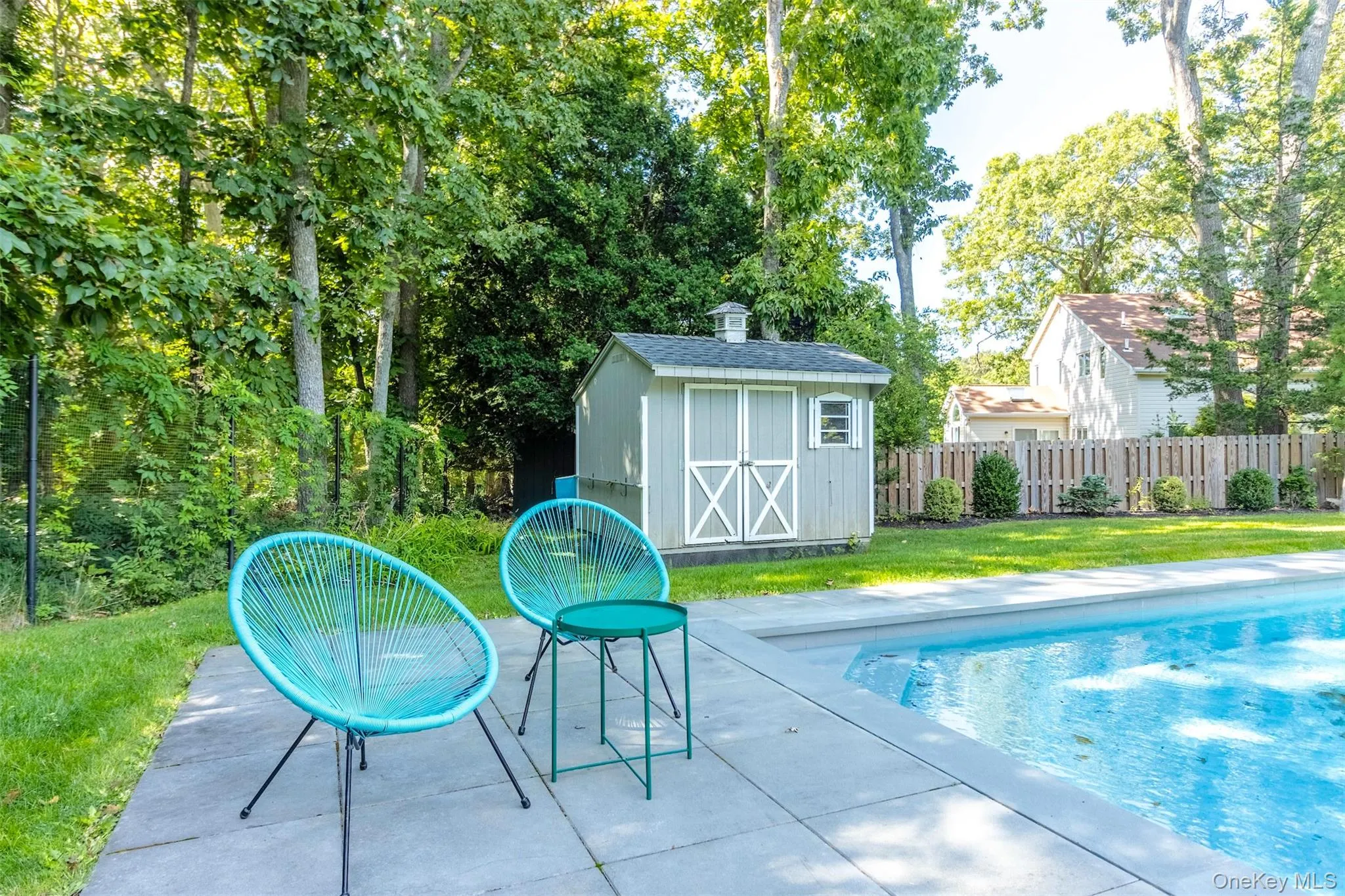 View of pool with a storage unit, a patio area, and view of wooded area View of pool with a storage unit, a patio area, and view of wooded area