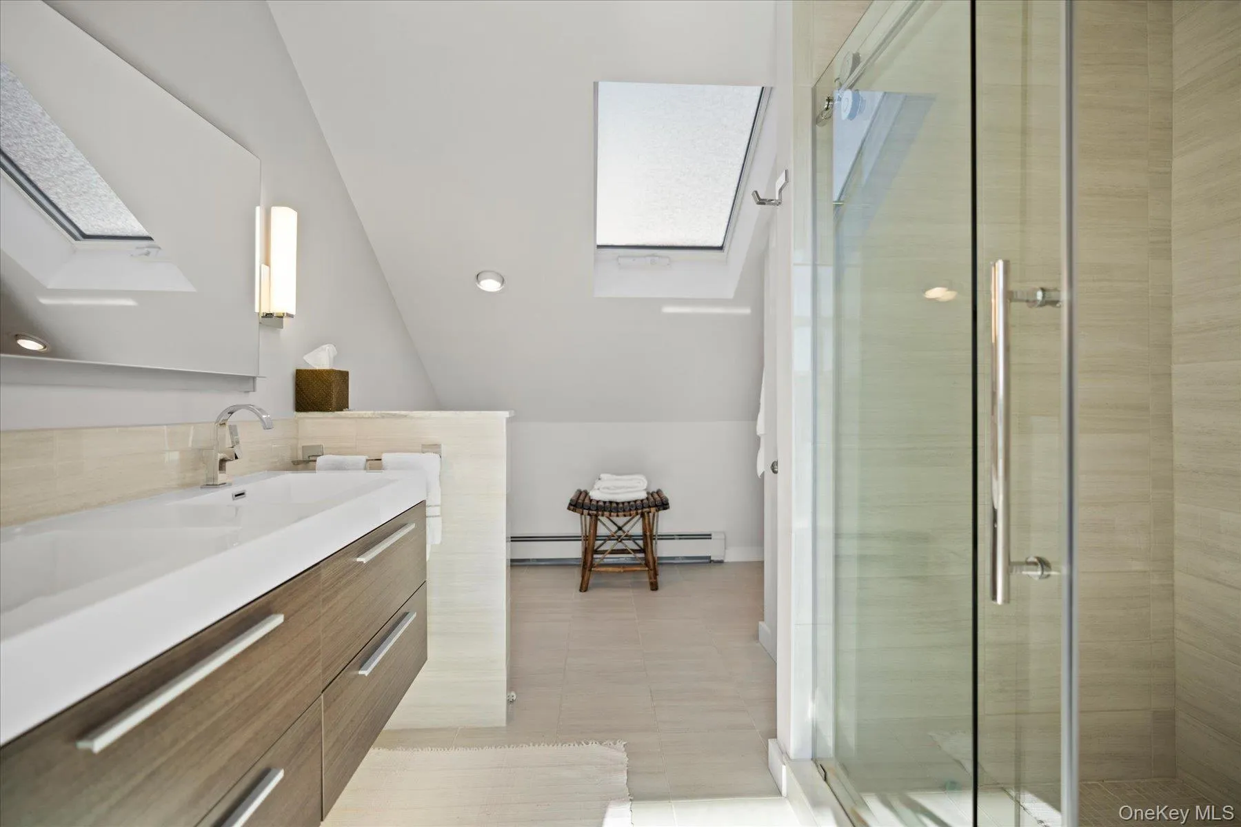 Primary ensuite Bathroom featuring baseboard heating, vaulted ceiling with skylight, a shower with shower door, and vanity Primary ensuite Bathroom featuring baseboard heating, vaulted ceiling with skylight, a shower with shower door, and vanity