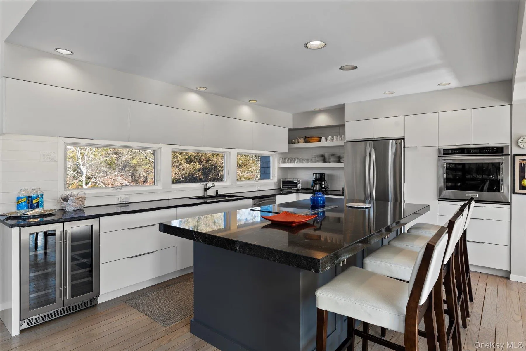 Kitchen with a kitchen breakfast bar, white cabinetry, a center island, beverage cooler, and stainless steel appliances Kitchen with a kitchen breakfast bar, white cabinetry, a center island, beverage cooler, and stainless steel appliances