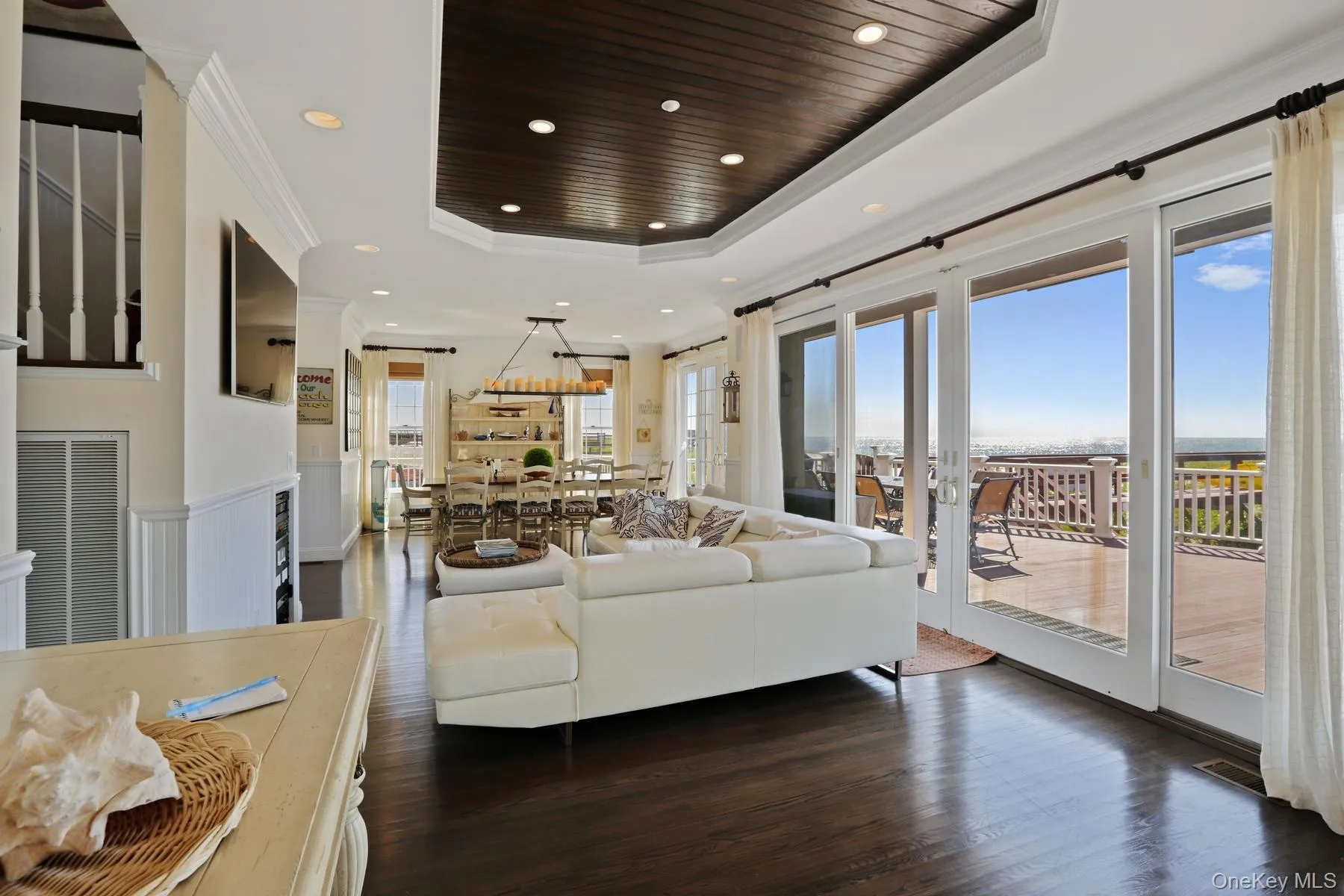 Living room with dark hardwood / wood-style floors, a raised ceiling, crown molding, wooden ceiling, and sliders to oceanfront deck Living room with dark hardwood / wood-style floors, a raised ceiling, crown molding, wooden ceiling, and sliders to oceanfront deck