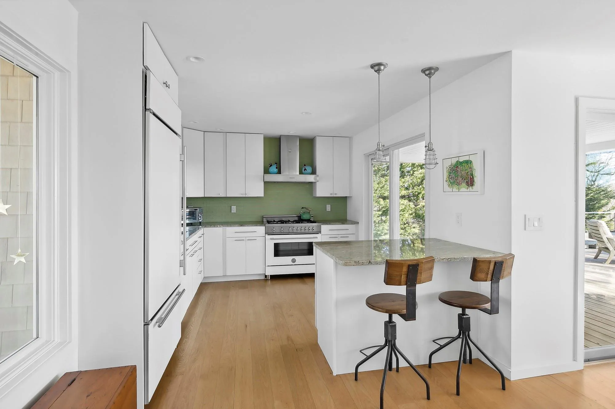 Kitchen featuring high end appliances, wall chimney exhaust hood, decorative light fixtures, white cabinetry, and kitchen peninsula Kitchen featuring high end appliances, wall chimney exhaust hood, decorative light fixtures, white cabinetry, and kitchen peninsula