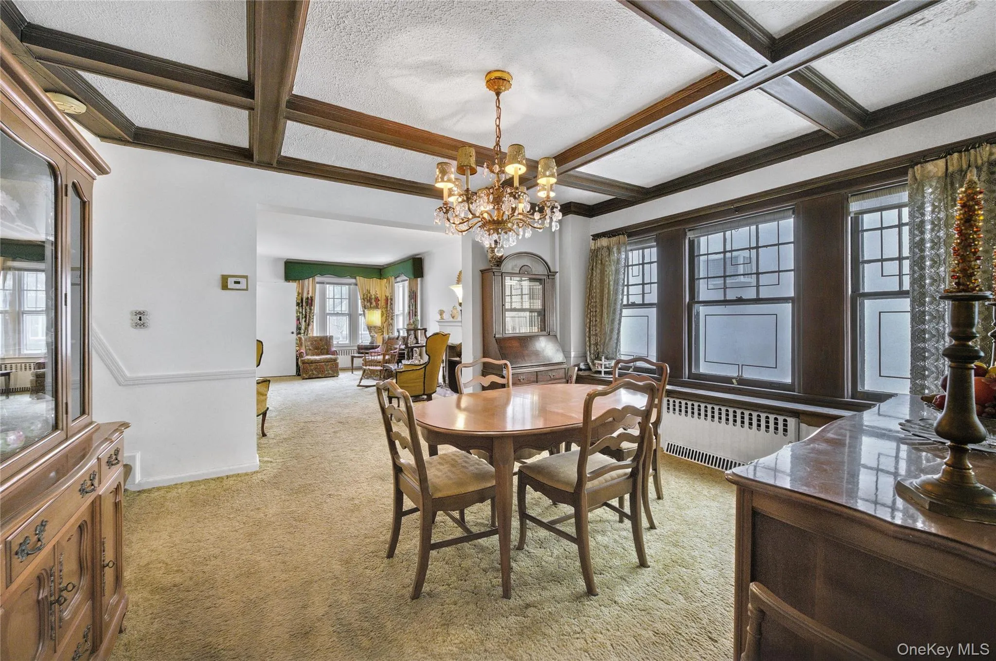 Carpeted dining room featuring an inviting chandelier, a textured ceiling, coffered ceiling, and radiator heating unit Carpeted dining room featuring an inviting chandelier, a textured ceiling, coffered ceiling, and radiator heating unit