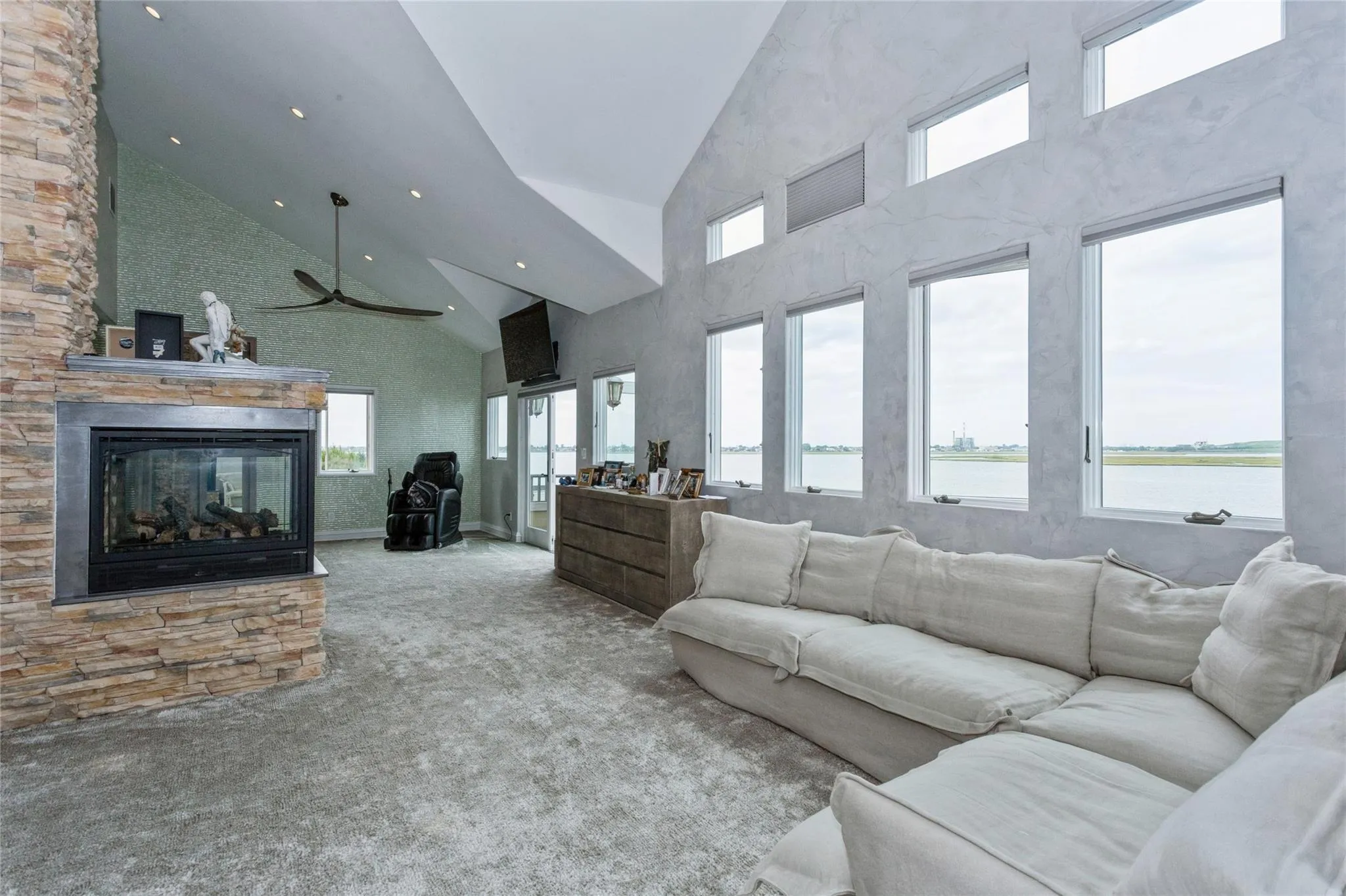 Carpeted living room with ceiling fan, a multi sided fireplace, and high vaulted ceiling Carpeted living room with ceiling fan, a multi sided fireplace, and high vaulted ceiling