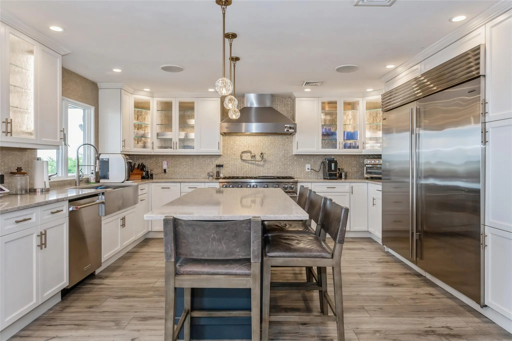 Kitchen with wall chimney exhaust hood, a center island, stainless steel appliances, and light stone counters Kitchen with wall chimney exhaust hood, a center island, stainless steel appliances, and light stone counters