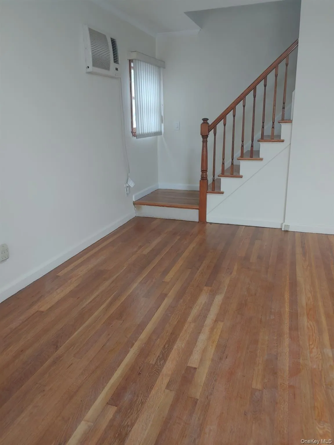 Unfurnished living room featuring hardwood / wood-style flooring, stairway, and an AC wall unit Unfurnished living room featuring hardwood / wood-style flooring, stairway, and an AC wall unit