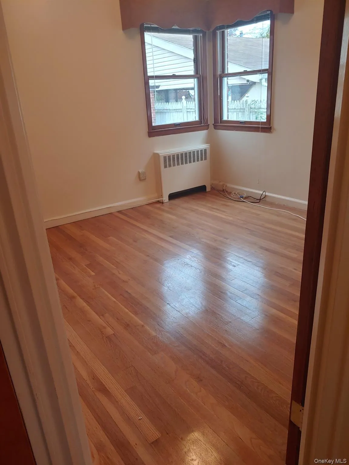 Empty room featuring light wood-style flooring, healthy amount of natural light, and radiator heating unit Empty room featuring light wood-style flooring, healthy amount of natural light, and radiator heating unit