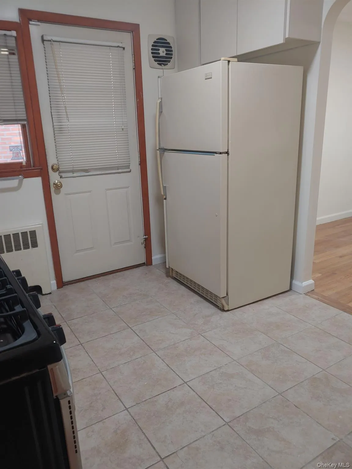 Kitchen featuring freestanding refrigerator, black gas range, radiator heating unit, arched walkways, and light tile patterned floors Kitchen featuring freestanding refrigerator, black gas range, radiator heating unit, arched walkways, and light tile patterned floors