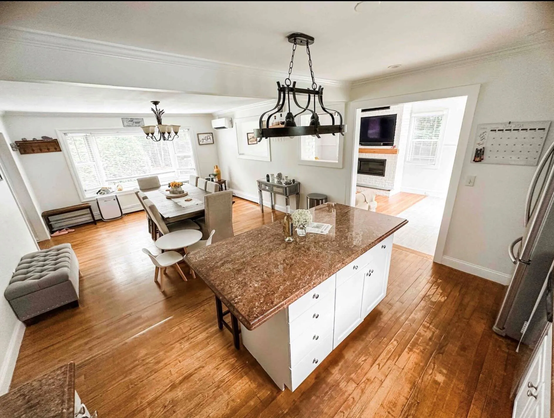 Kitchen with white cabinets, a kitchen island, wood finished floors, dark stone countertops, and decorative light fixtures Kitchen with white cabinets, a kitchen island, wood finished floors, dark stone countertops, and decorative light fixtures