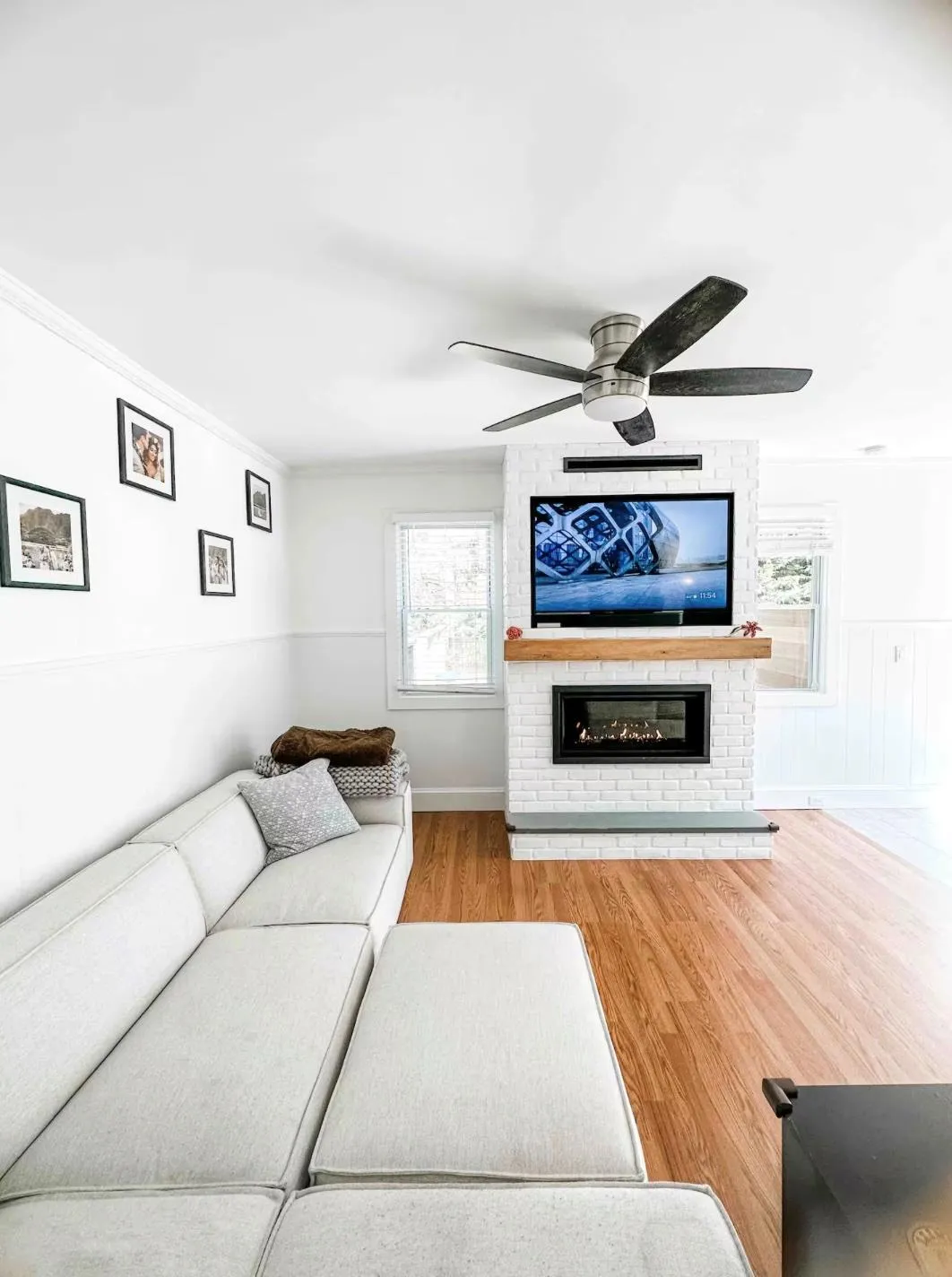 Living area featuring ceiling fan, a large fireplace, ornamental molding, wainscoting, and light wood finished floors Living area featuring ceiling fan, a large fireplace, ornamental molding, wainscoting, and light wood finished floors