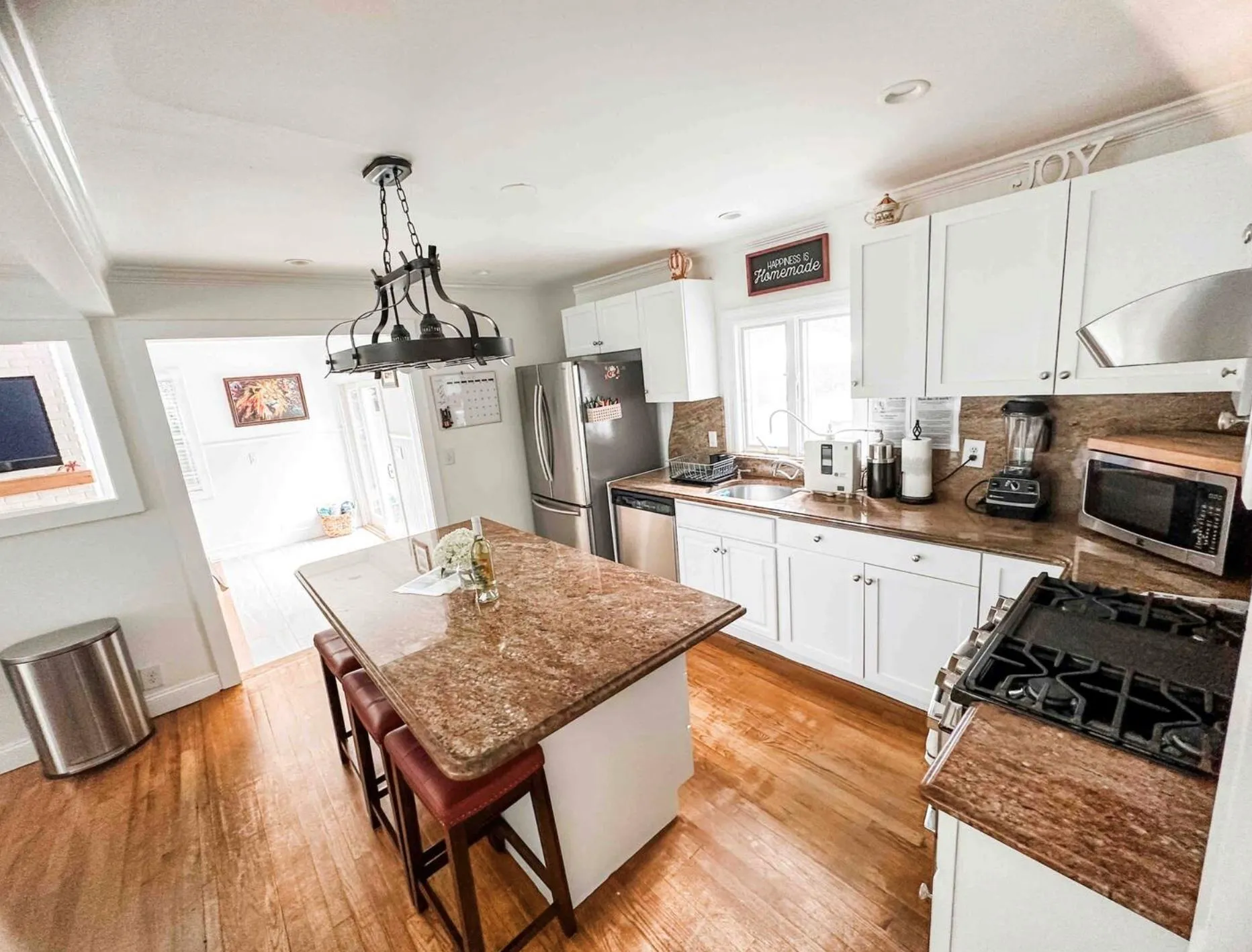 Kitchen featuring light wood finished floors, a kitchen island, decorative light fixtures, stainless steel appliances, and white cabinetry Kitchen featuring light wood finished floors, a kitchen island, decorative light fixtures, stainless steel appliances, and white cabinetry