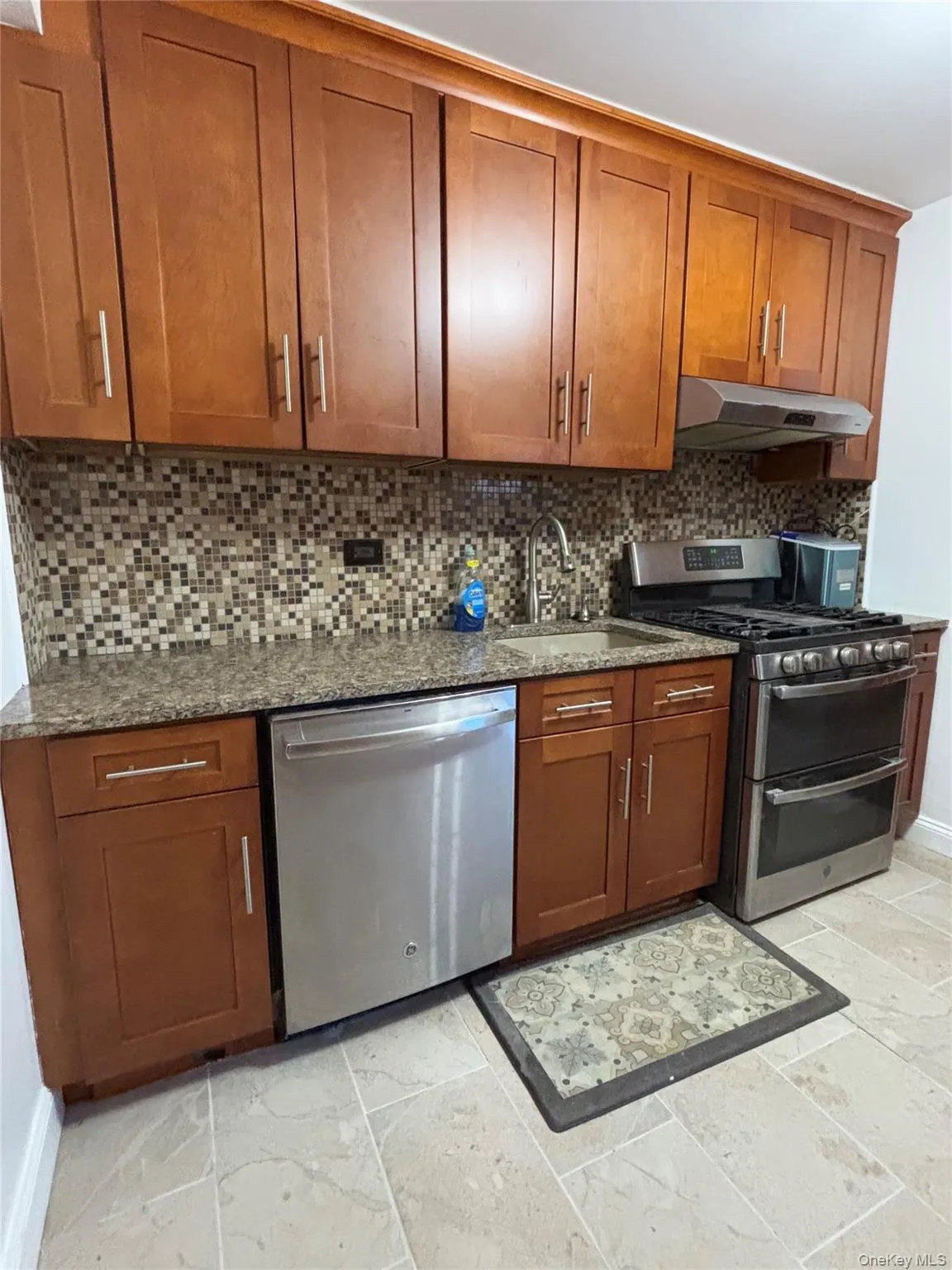 Kitchen with dark stone counters, appliances with stainless steel finishes, brown cabinets, under cabinet range hood, and a sink Kitchen with dark stone counters, appliances with stainless steel finishes, brown cabinets, under cabinet range hood, and a sink