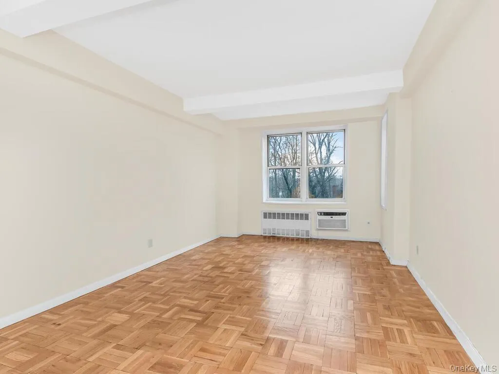 Spare room with radiator heating unit, baseboards, an AC wall unit, and beamed ceiling Spare room with radiator heating unit, baseboards, an AC wall unit, and beamed ceiling