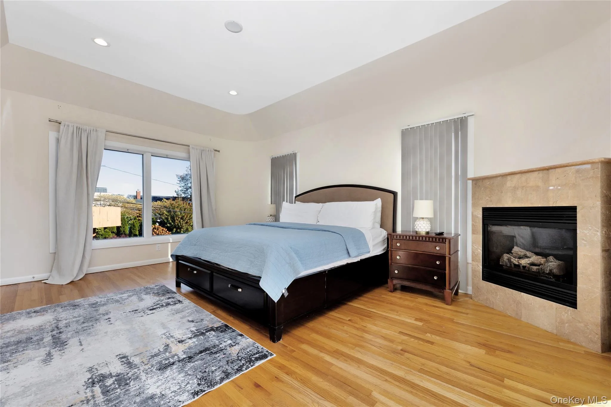 Bedroom with light wood finished floors, baseboards, a tiled fireplace, and recessed lighting Bedroom with light wood finished floors, baseboards, a tiled fireplace, and recessed lighting