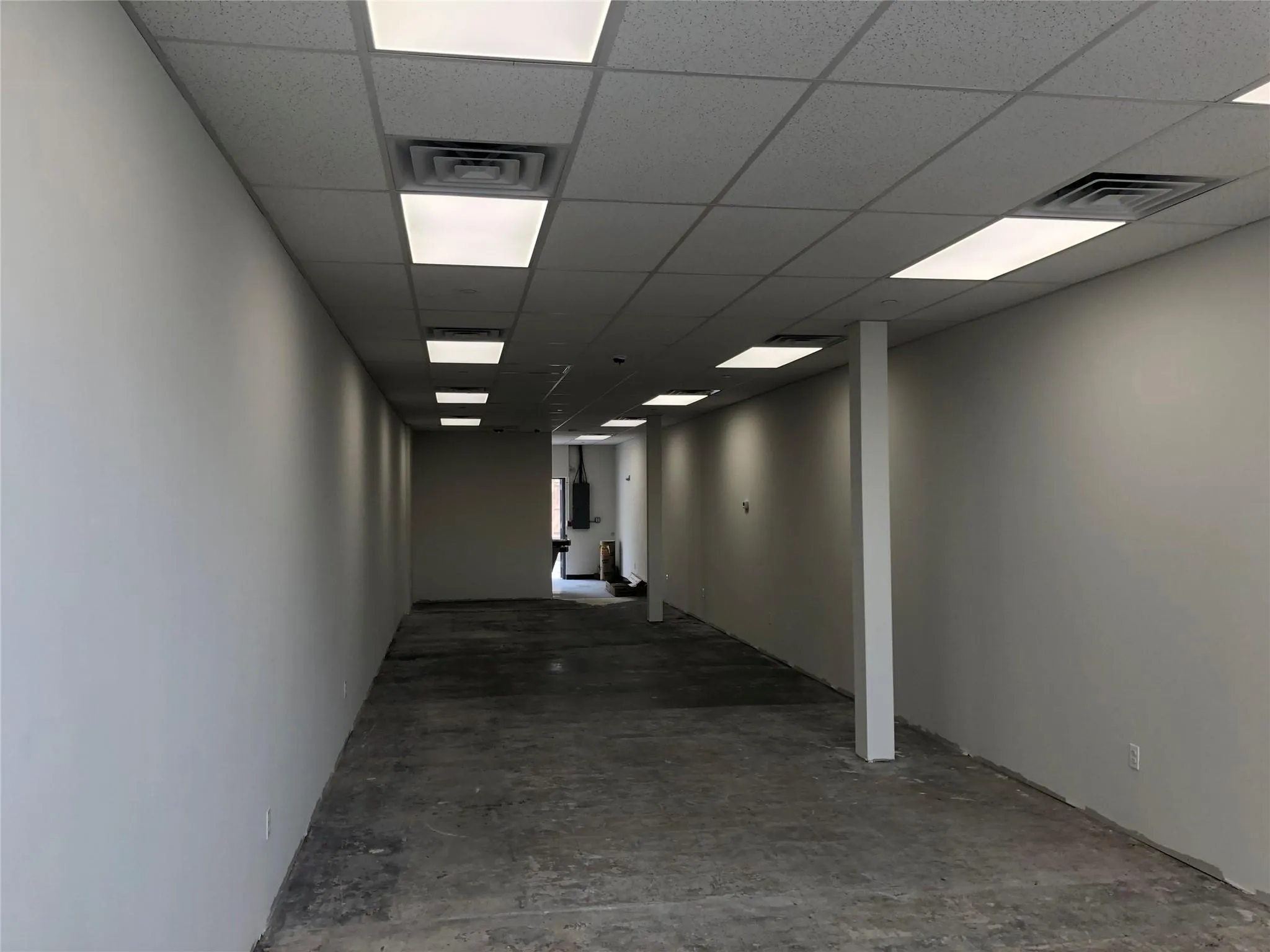 Hallway featuring a paneled ceiling, concrete floors, and visible vents Hallway featuring a paneled ceiling, concrete floors, and visible vents