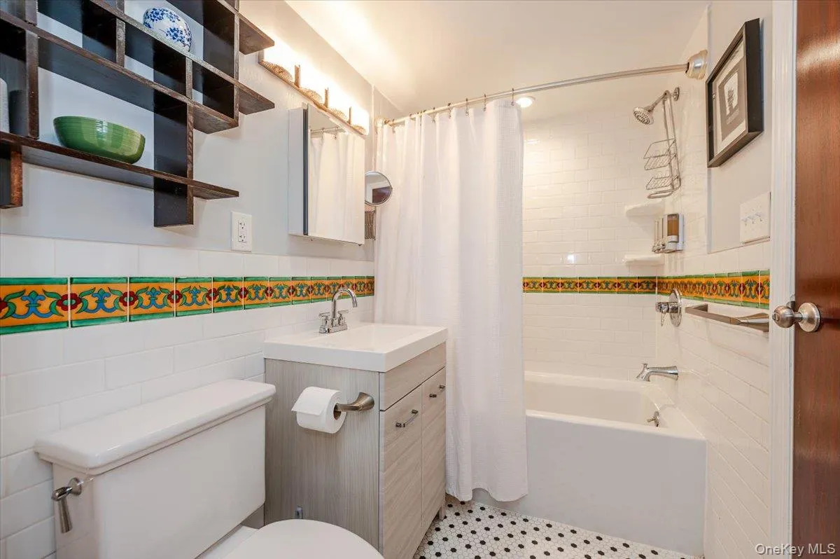 Full Bathroom with toilet, vanity, tile walls, wainscoting, and shower/tub combo Full Bathroom with toilet, vanity, tile walls, wainscoting, and shower/tub combo