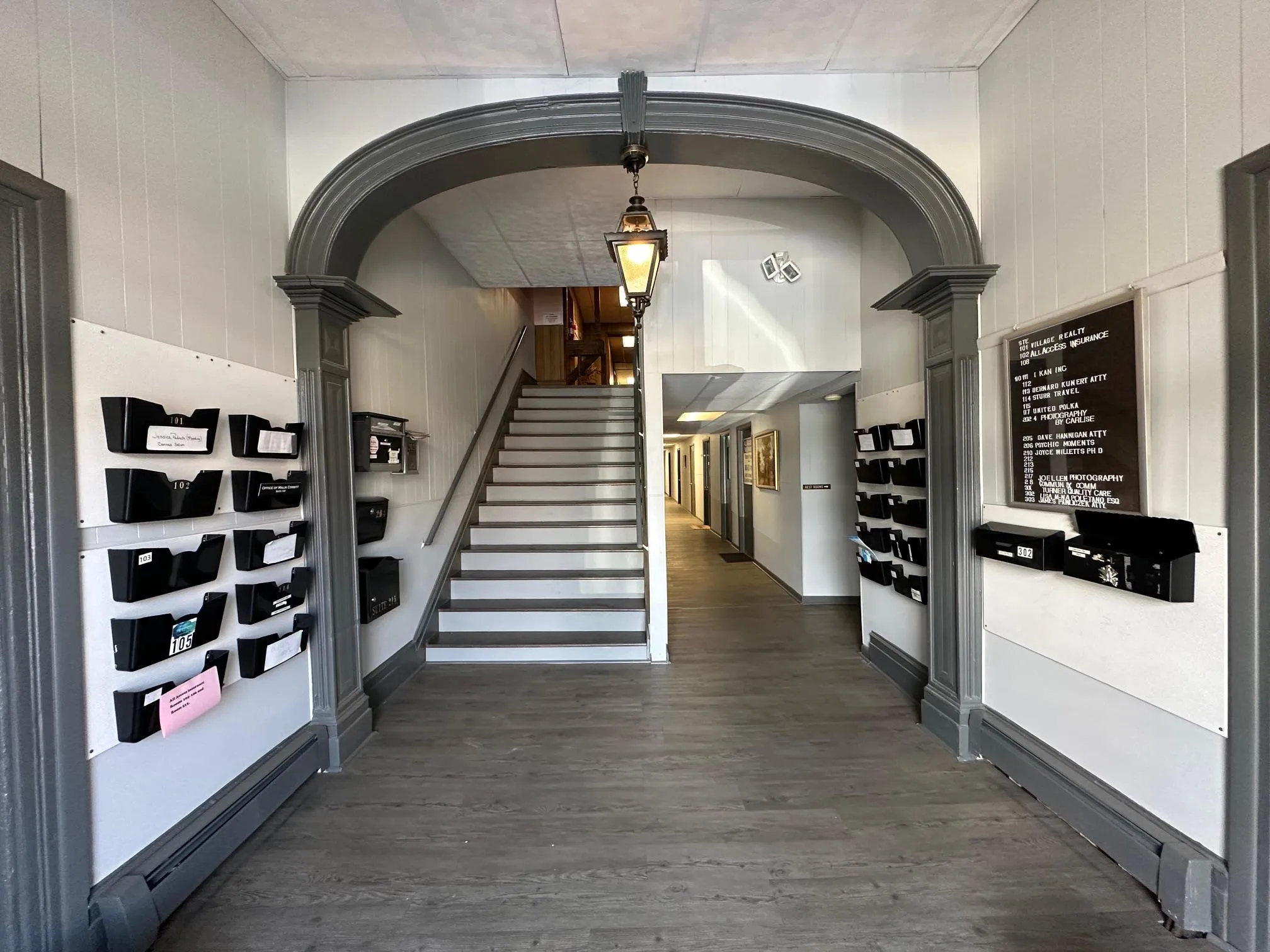 Hall with arched walkways, wood walls, stairs, dark wood-style floors, and ornate columns Hall with arched walkways, wood walls, stairs, dark wood-style floors, and ornate columns