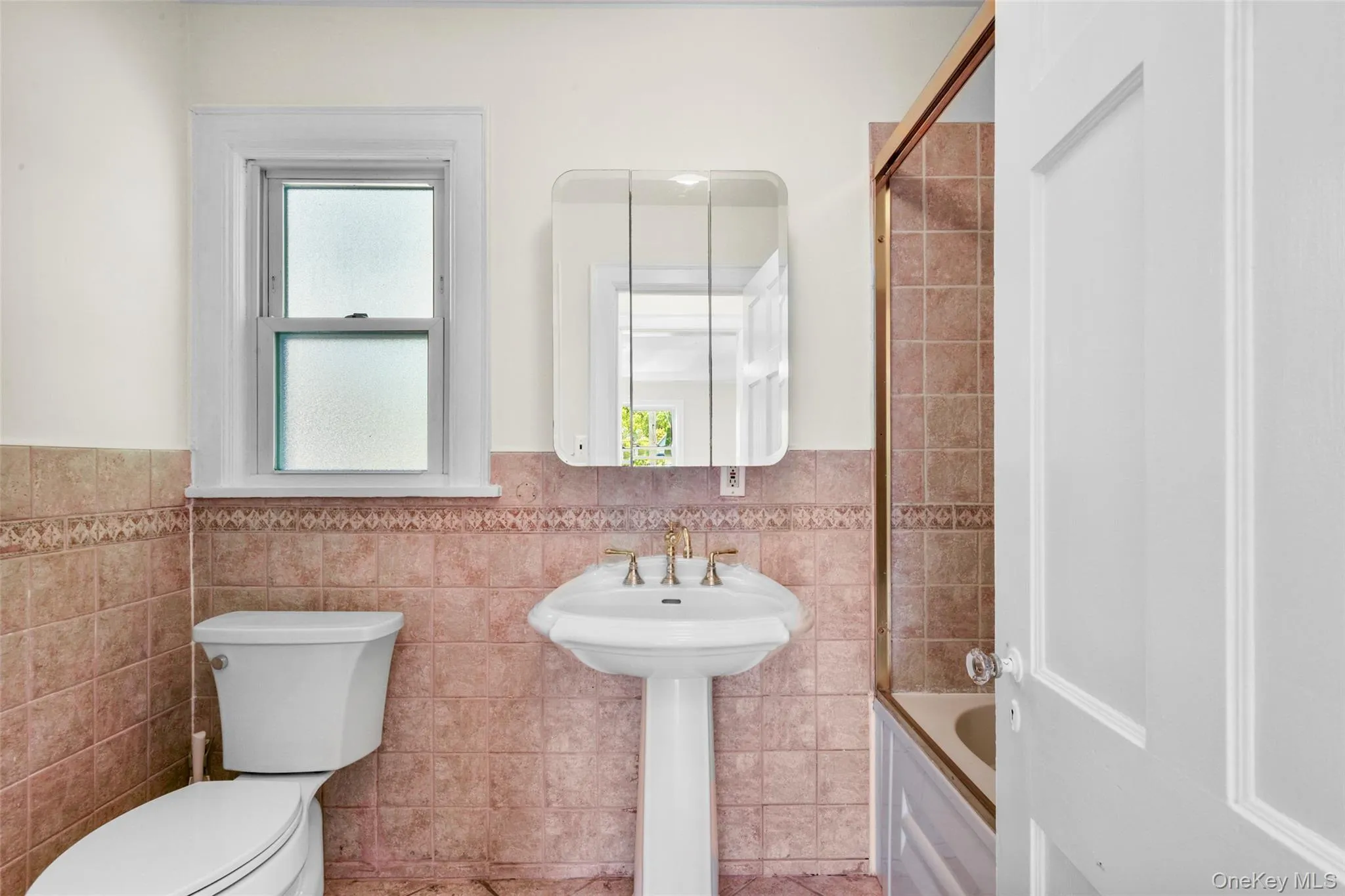 Full bath with wainscoting, tile walls, and shower / bath combination with glass door Full bath with wainscoting, tile walls, and shower / bath combination with glass door