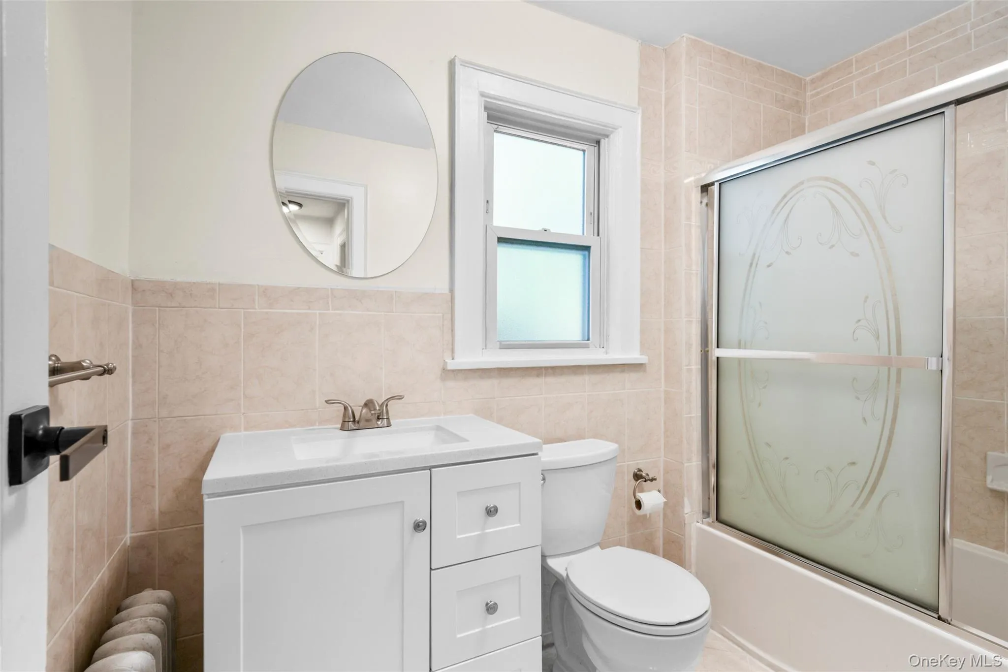 Full bathroom featuring shower / bath combination with glass door, vanity, tile walls, and radiator Full bathroom featuring shower / bath combination with glass door, vanity, tile walls, and radiator