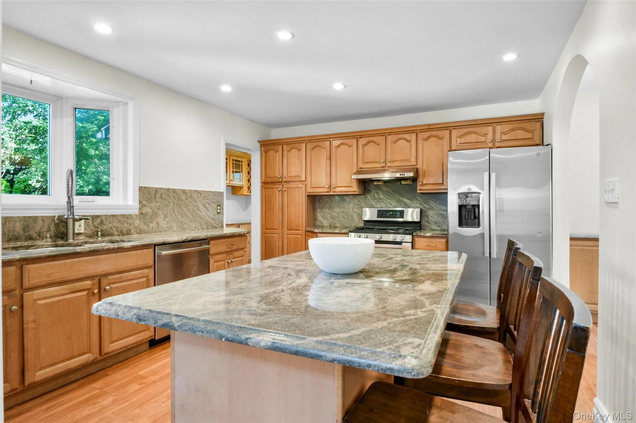 Kitchen with a kitchen bar, appliances with stainless steel finishes, a center island, light stone counters, and arched walkways Kitchen with a kitchen bar, appliances with stainless steel finishes, a center island, light stone counters, and arched walkways