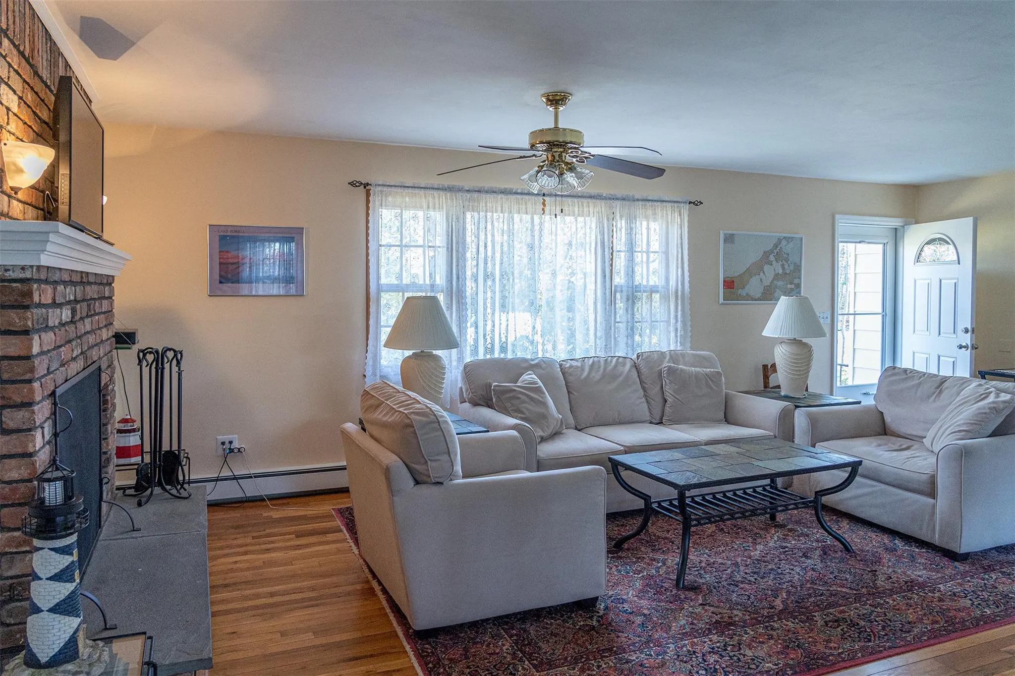 Living area featuring a baseboard heating unit, a fireplace, ceiling fan, and wood finished floors Living area featuring a baseboard heating unit, a fireplace, ceiling fan, and wood finished floors