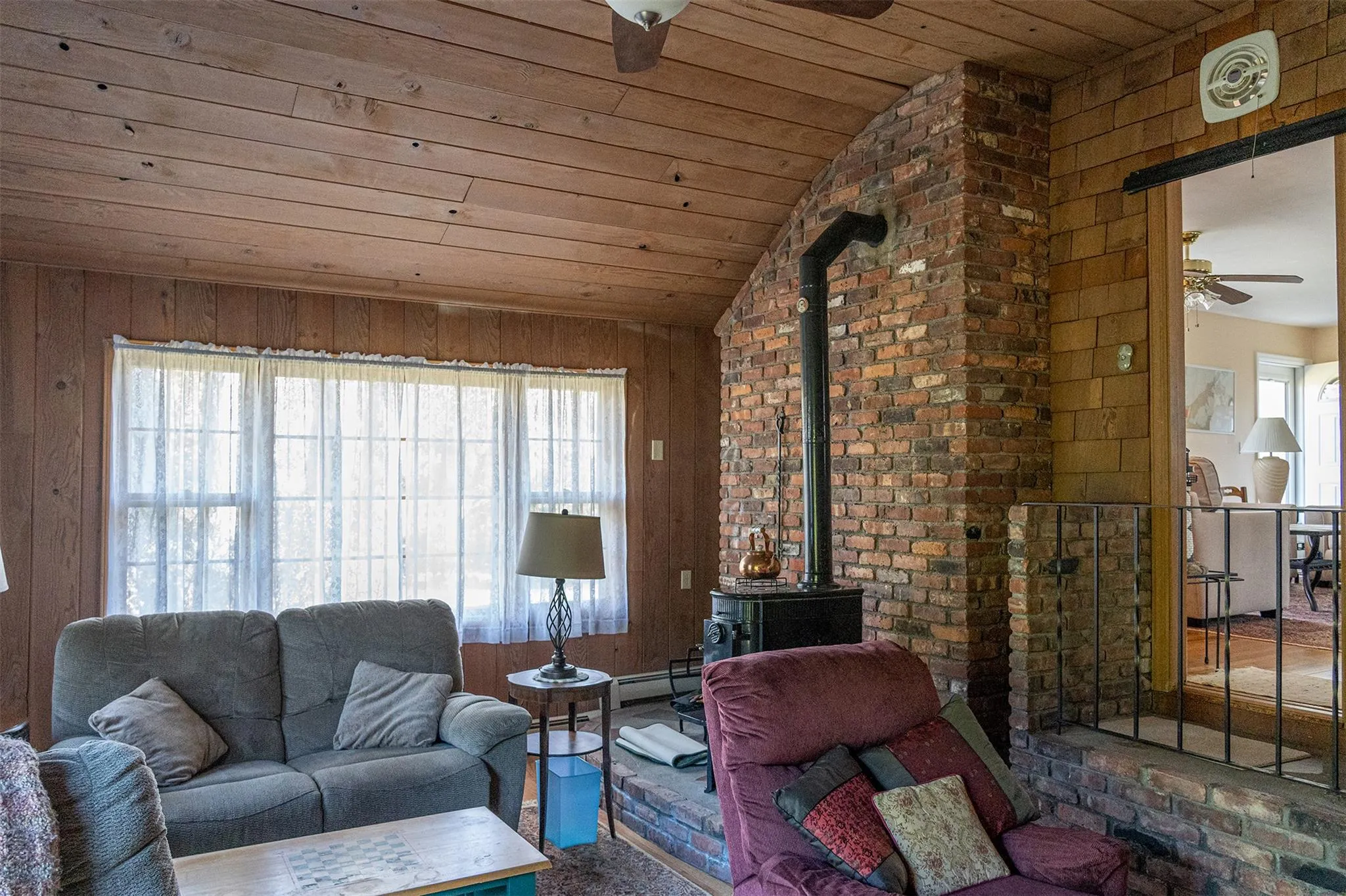 Living area featuring lofted ceiling, ceiling fan, wooden ceiling, wooden walls, and a wood stove Living area featuring lofted ceiling, ceiling fan, wooden ceiling, wooden walls, and a wood stove