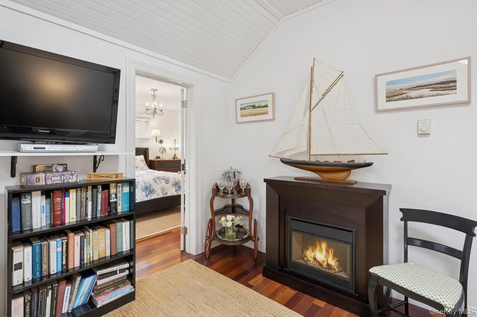 Living area featuring lofted ceiling, a notable chandelier, wood finished floors, and a glass covered fireplace Living area featuring lofted ceiling, a notable chandelier, wood finished floors, and a glass covered fireplace