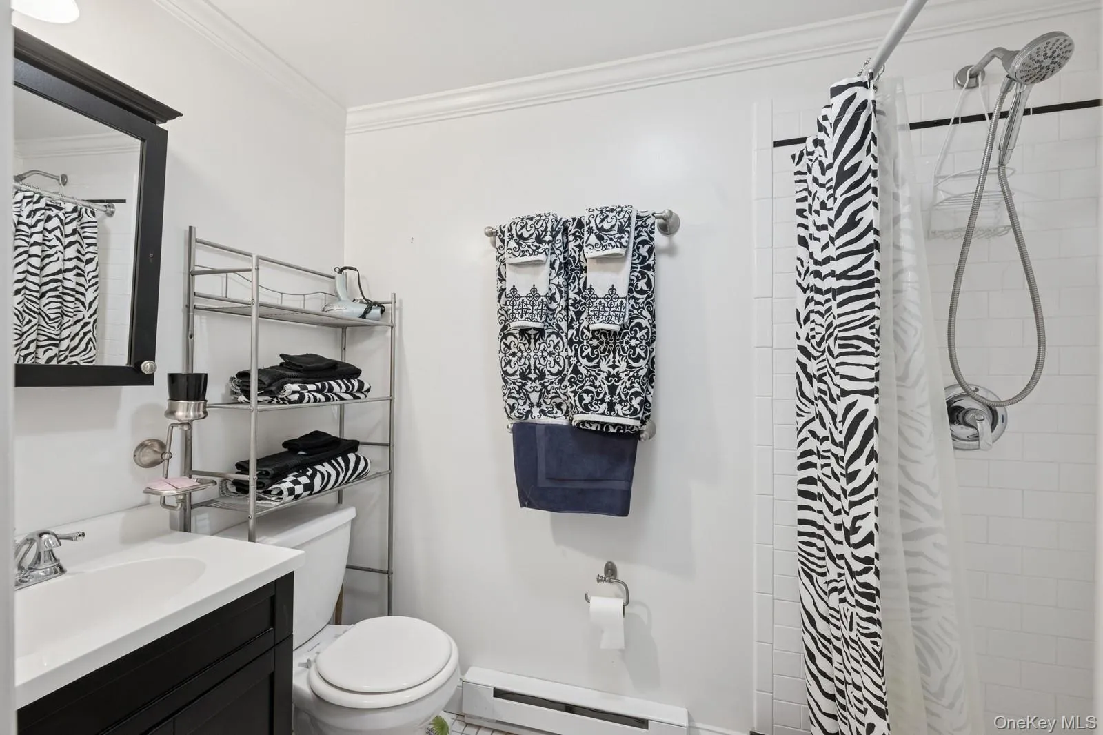 Bathroom with a baseboard radiator, toilet, vanity, ornamental molding, and tiled shower Bathroom with a baseboard radiator, toilet, vanity, ornamental molding, and tiled shower