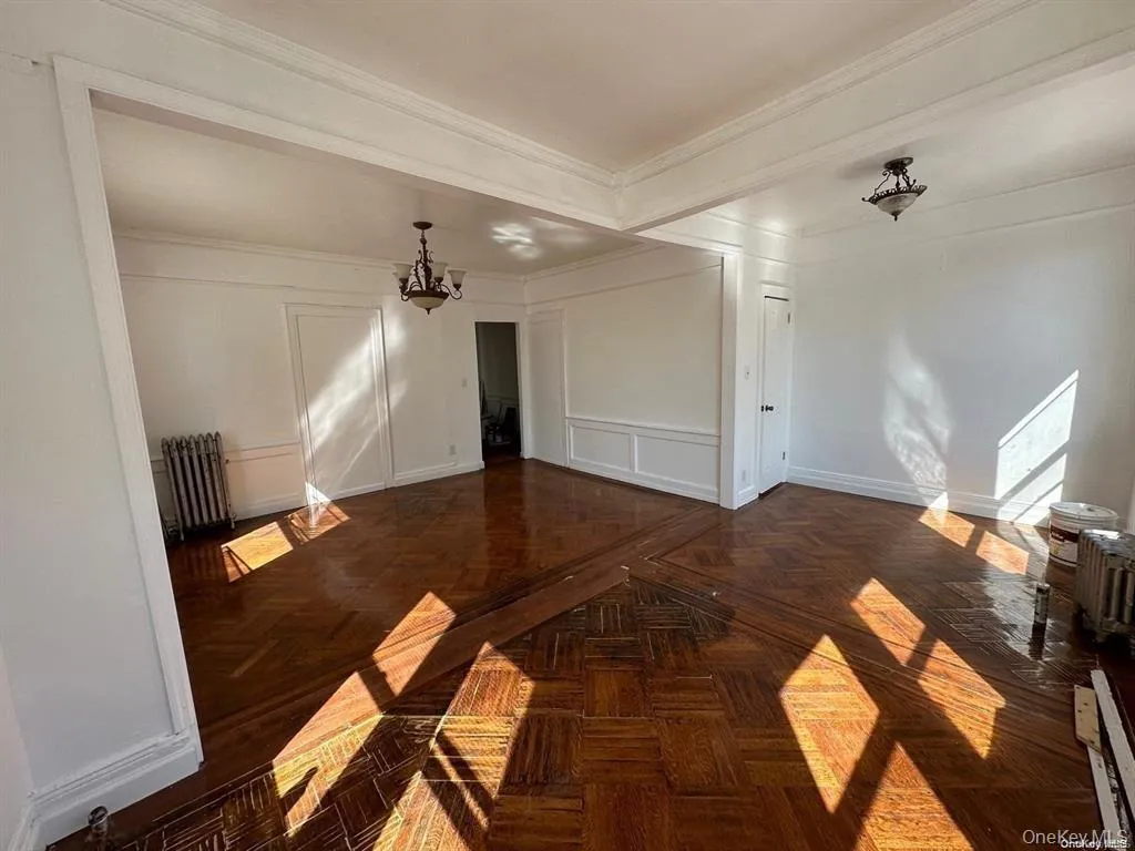 Spare room featuring a chandelier, radiator, a decorative wall, and ornamental molding Spare room featuring a chandelier, radiator, a decorative wall, and ornamental molding