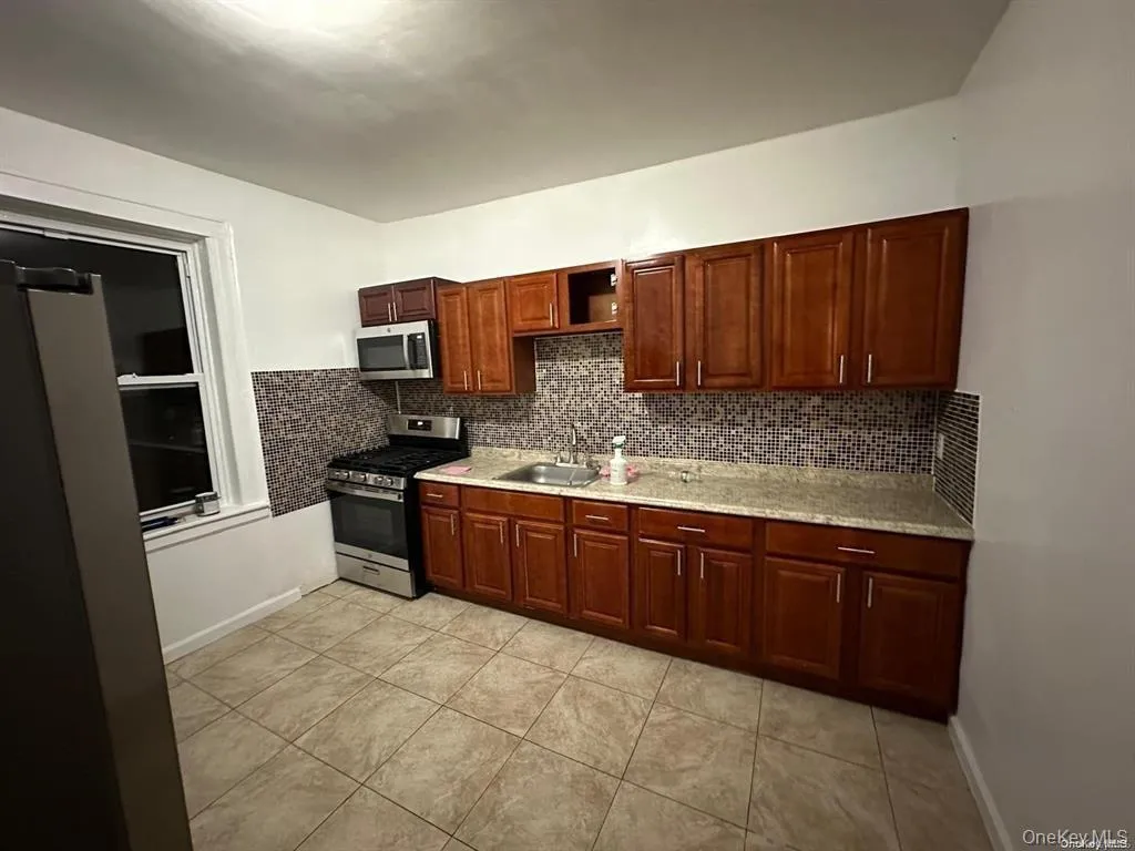 Kitchen featuring appliances with stainless steel finishes, light tile patterned flooring, a sink, and tasteful backsplash Kitchen featuring appliances with stainless steel finishes, light tile patterned flooring, a sink, and tasteful backsplash