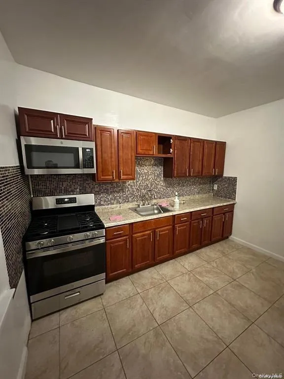 Kitchen with light tile patterned floors, appliances with stainless steel finishes, a sink, open shelves, and backsplash Kitchen with light tile patterned floors, appliances with stainless steel finishes, a sink, open shelves, and backsplash