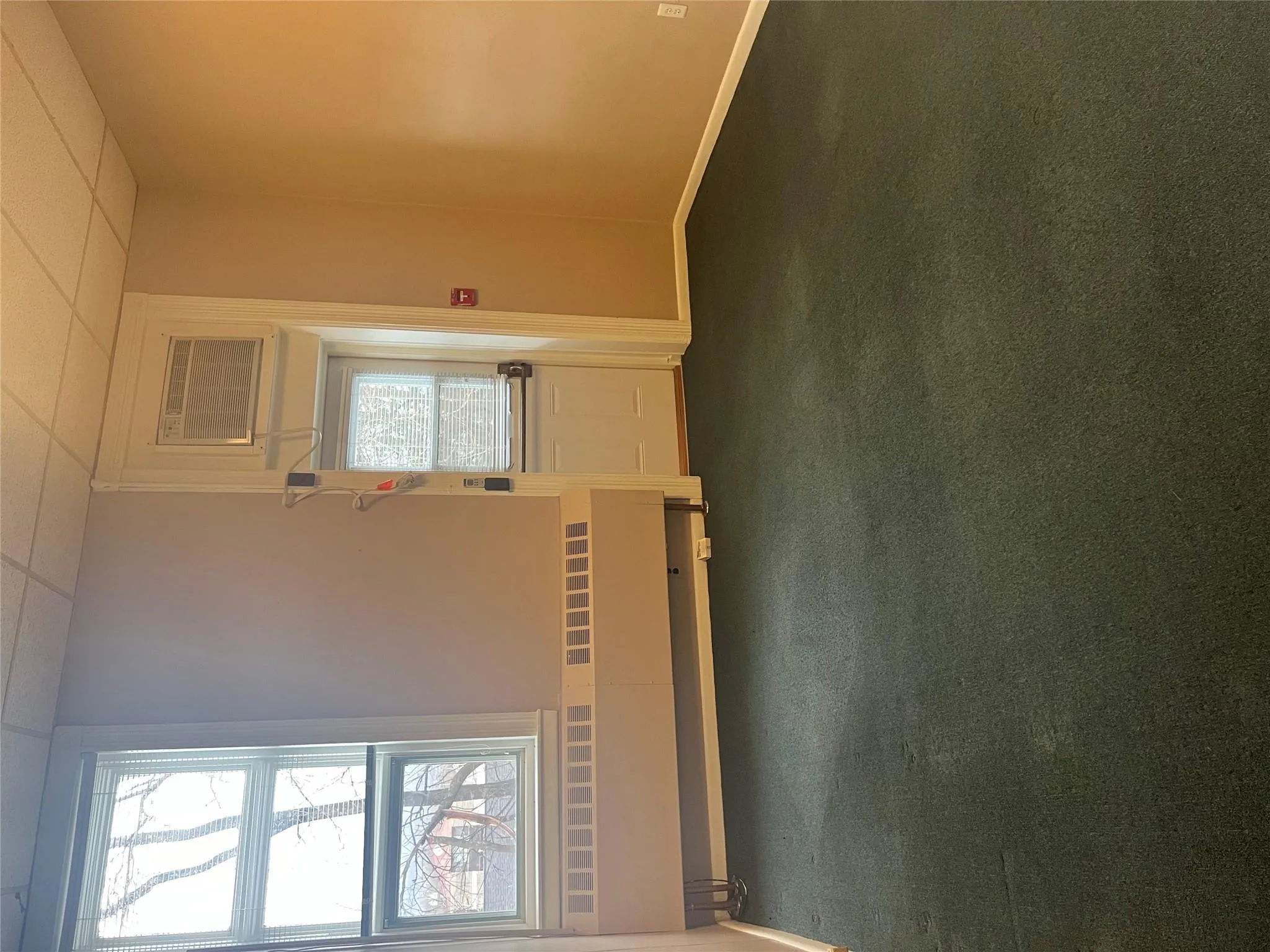 Empty room featuring baseboards, a wall mounted air conditioner, dark carpet, and a drop ceiling Empty room featuring baseboards, a wall mounted air conditioner, dark carpet, and a drop ceiling