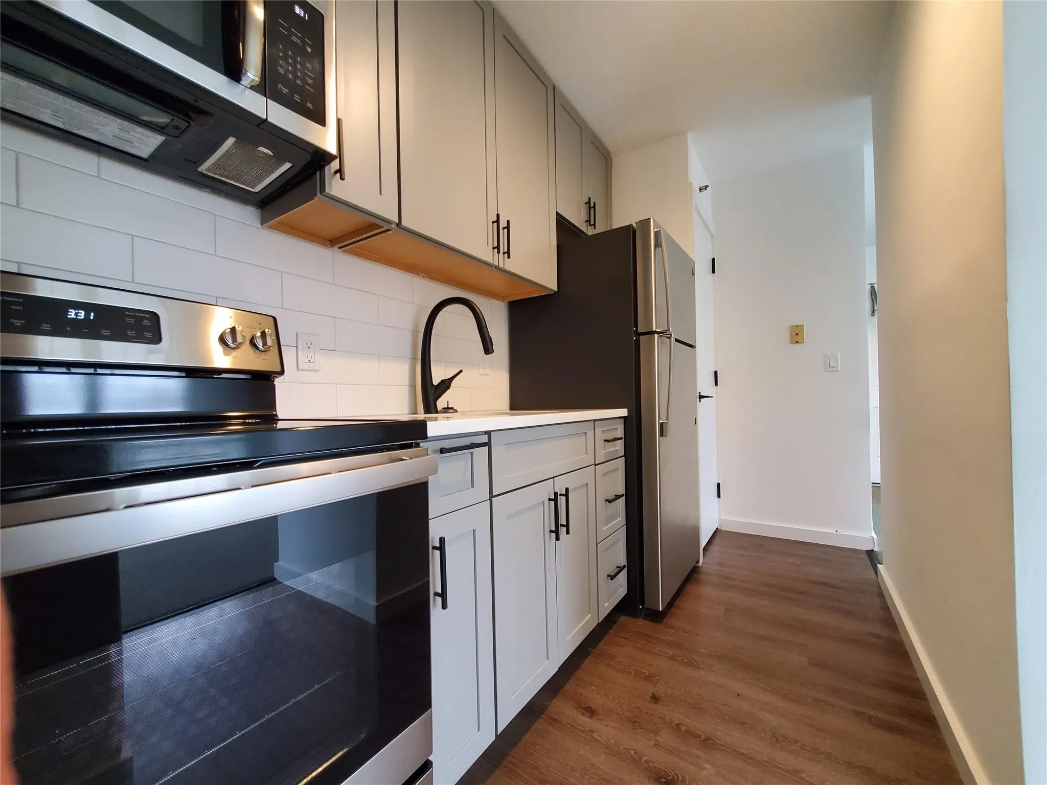 Kitchen featuring dark wood-type flooring, baseboards, gray cabinetry, backsplash, and appliances with stainless steel finishes Kitchen featuring dark wood-type flooring, baseboards, gray cabinetry, backsplash, and appliances with stainless steel finishes