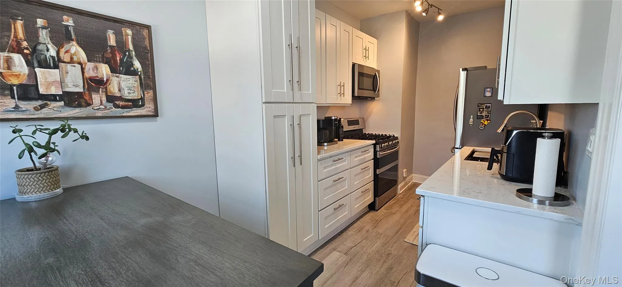 Kitchen with stainless steel appliances, light wood-style floors, white cabinets, light stone countertops, and track lighting Kitchen with stainless steel appliances, light wood-style floors, white cabinets, light stone countertops, and track lighting