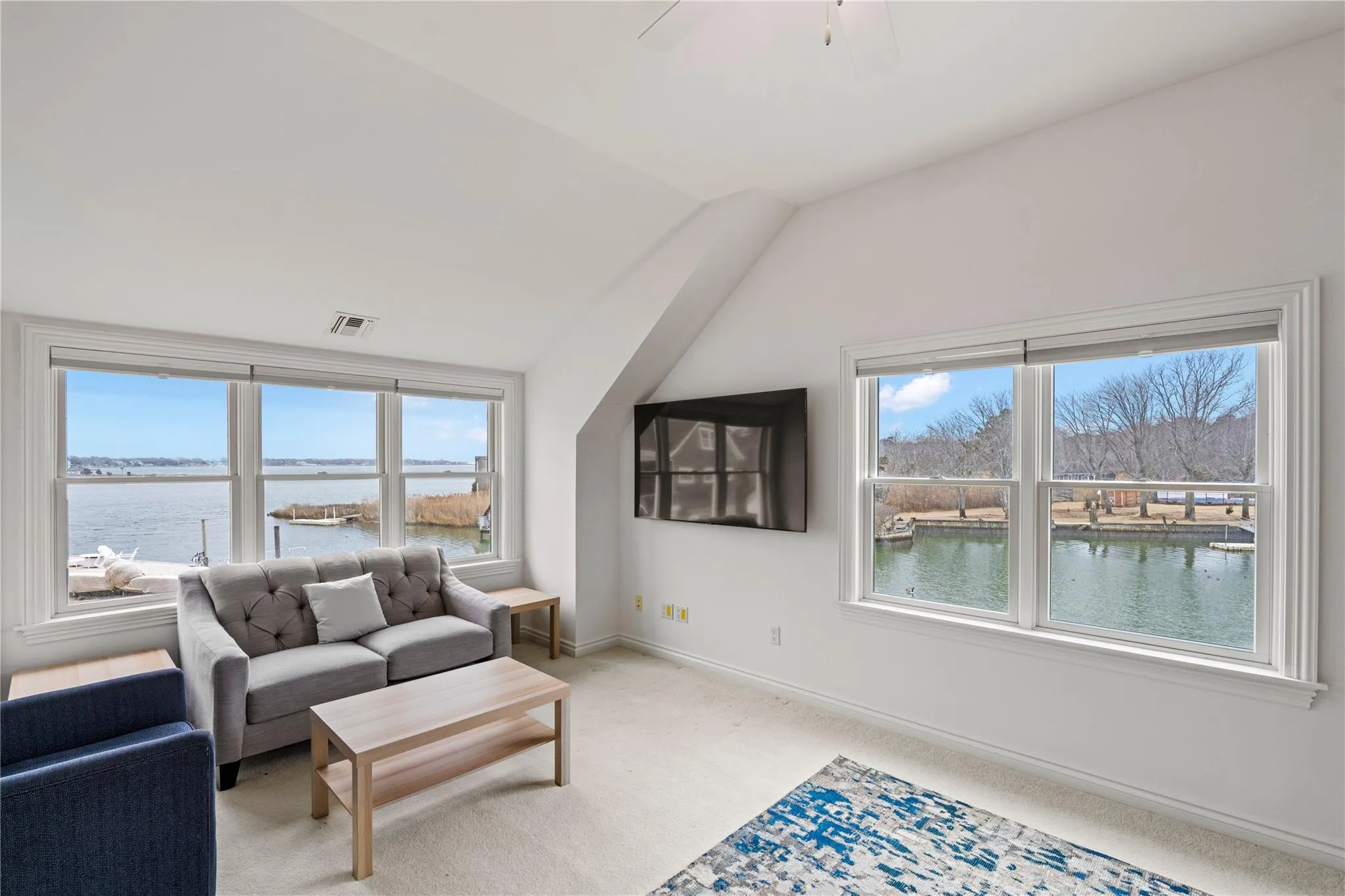 Living room with light colored carpet, a water view, visible vents, baseboards, and vaulted ceiling Living room with light colored carpet, a water view, visible vents, baseboards, and vaulted ceiling
