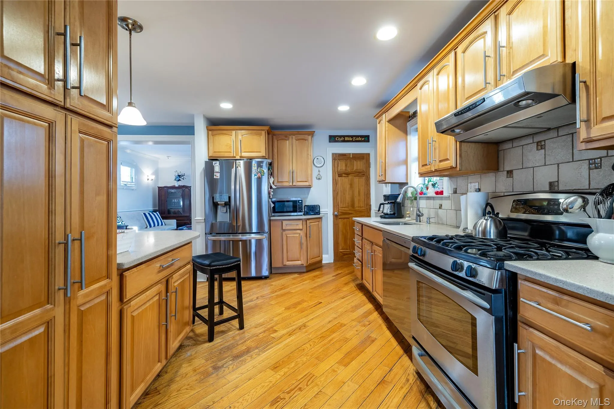 Kitchen with light wood finished floors, stainless steel appliances, light countertops, a sink, and under cabinet range hood Kitchen with light wood finished floors, stainless steel appliances, light countertops, a sink, and under cabinet range hood