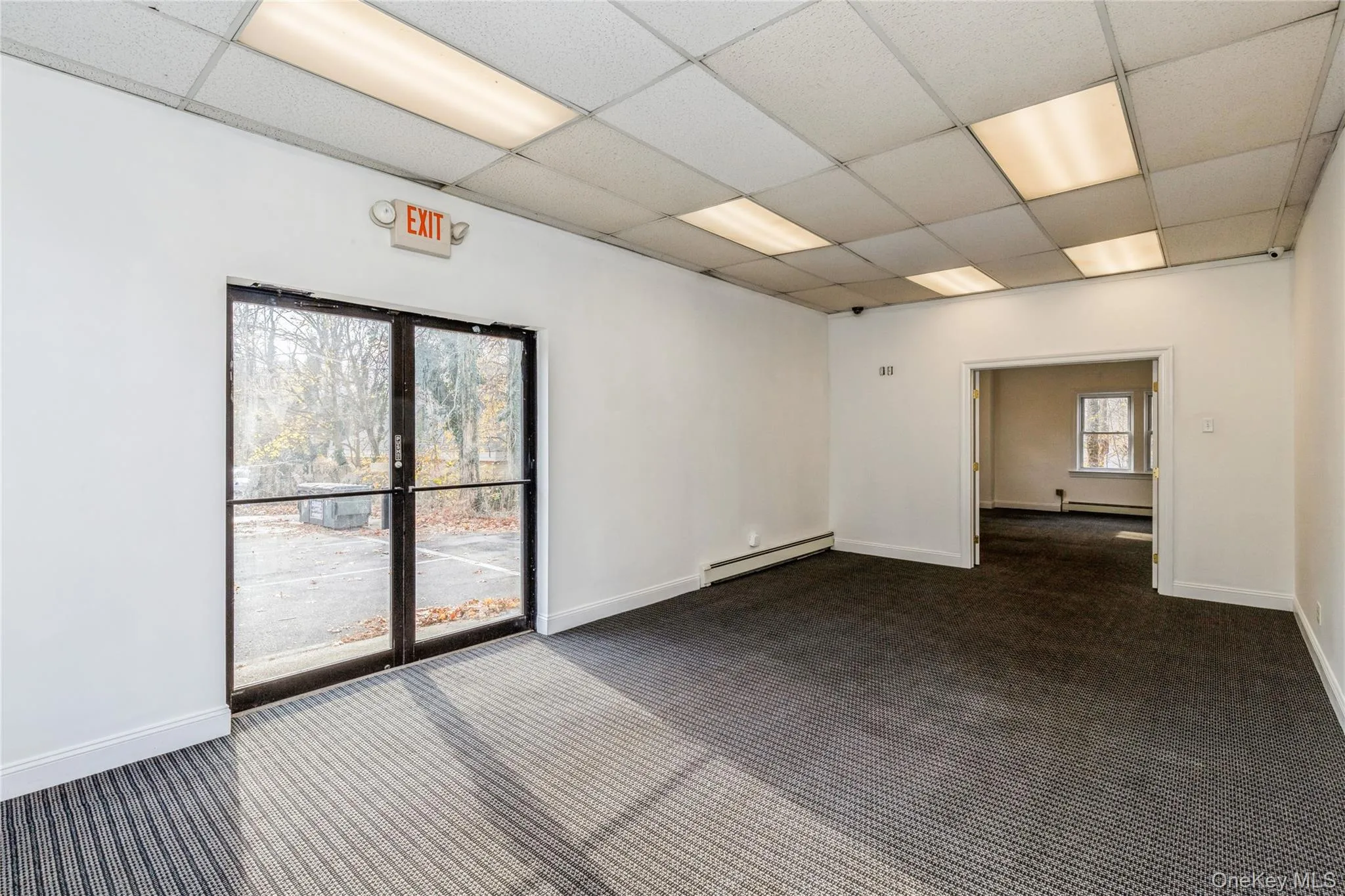 Empty room with a baseboard heating unit, a paneled ceiling, dark carpet, and baseboards Empty room with a baseboard heating unit, a paneled ceiling, dark carpet, and baseboards