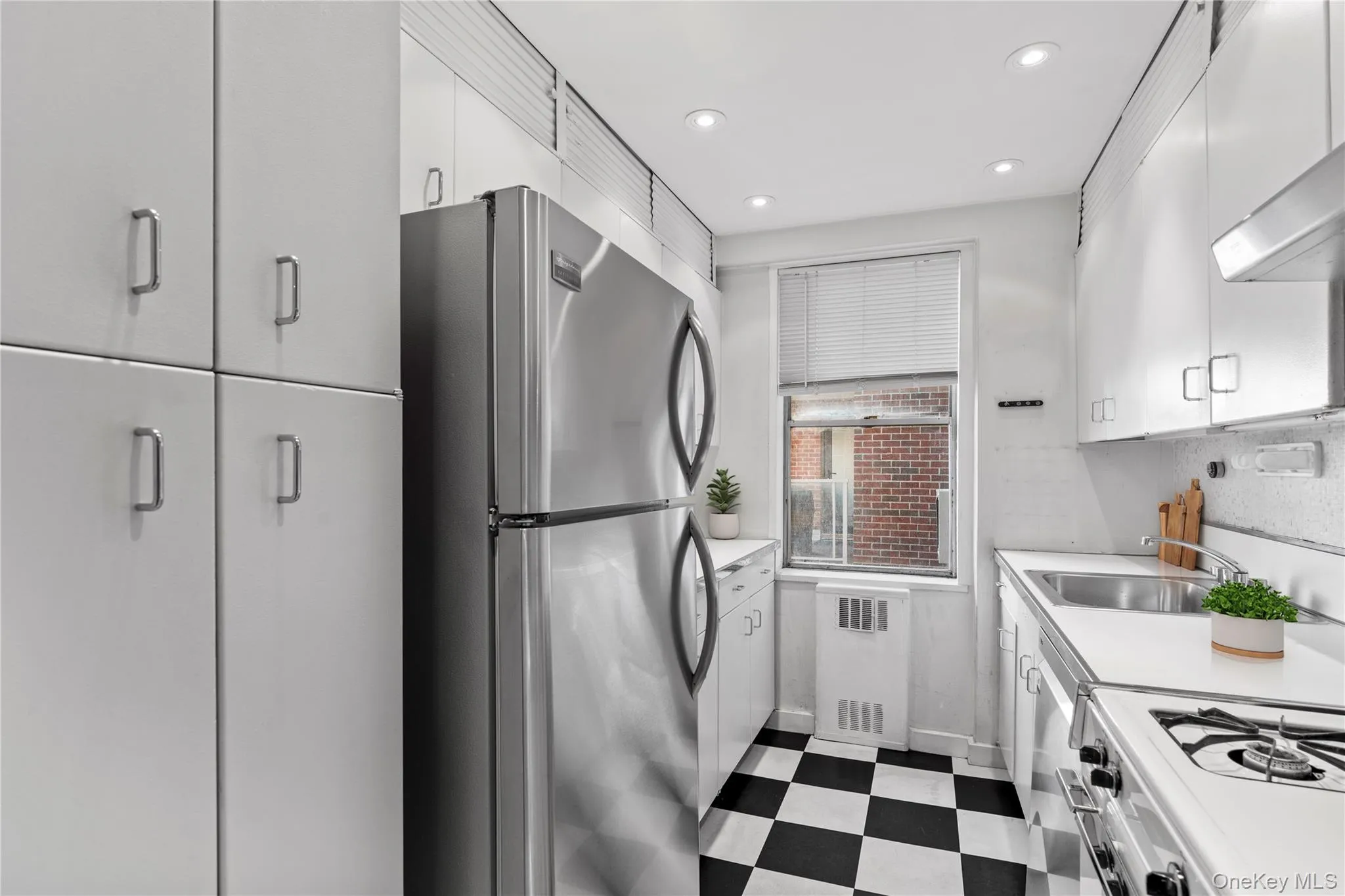 Kitchen featuring a sink, freestanding refrigerator, radiator, dark floors, and light countertops Kitchen featuring a sink, freestanding refrigerator, radiator, dark floors, and light countertops