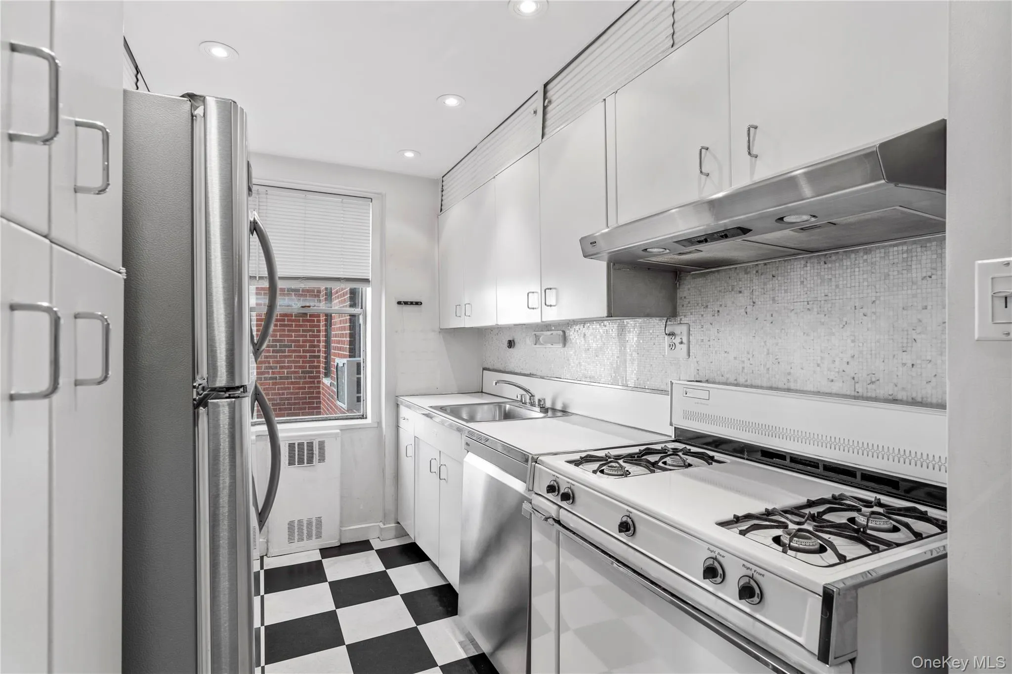 Kitchen with light floors, a sink, appliances with stainless steel finishes, under cabinet range hood, and white cabinetry Kitchen with light floors, a sink, appliances with stainless steel finishes, under cabinet range hood, and white cabinetry