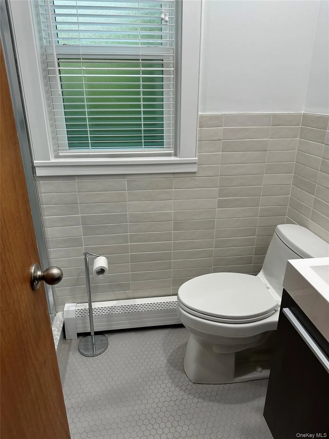 Half bath with tile walls, toilet, a baseboard heating unit, vanity, and tile patterned floors Half bath with tile walls, toilet, a baseboard heating unit, vanity, and tile patterned floors