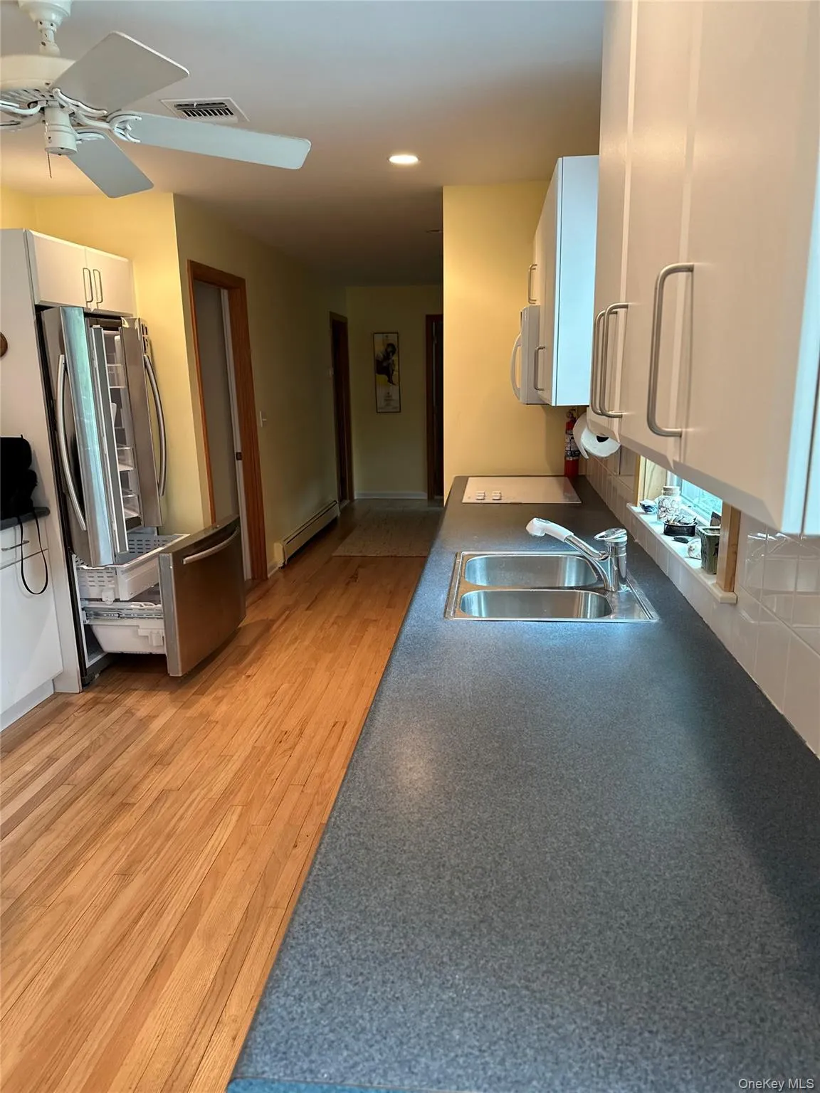 Kitchen with visible vents, white cabinets, white microwave, a baseboard radiator, and a sink Kitchen with visible vents, white cabinets, white microwave, a baseboard radiator, and a sink