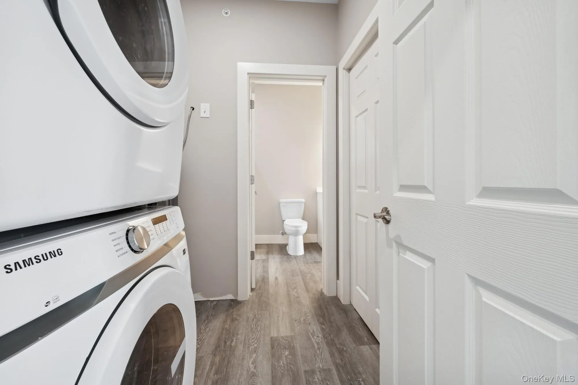 Laundry area with stacked washer and clothes dryer and dark wood-type flooring Laundry area with stacked washer and clothes dryer and dark wood-type flooring