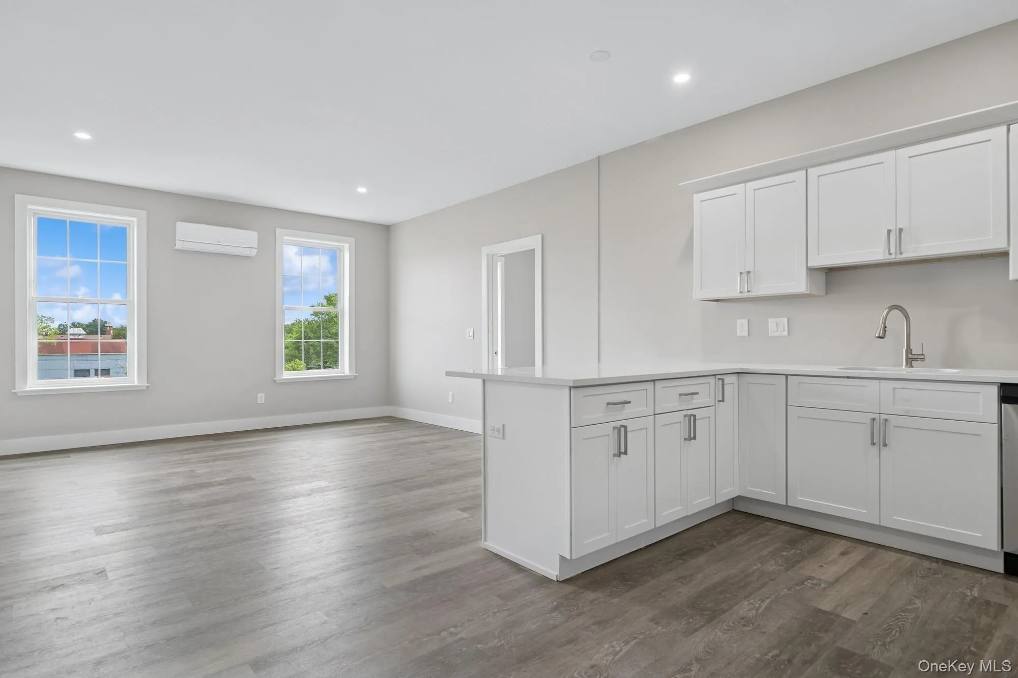 Kitchen with a peninsula, a wall mounted air conditioner, light countertops, dark wood-style floors, and recessed lighting Kitchen with a peninsula, a wall mounted air conditioner, light countertops, dark wood-style floors, and recessed lighting